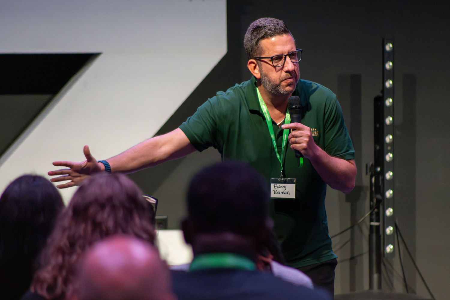 Speaker presenting on stage at a professional conference with dark backdrop.