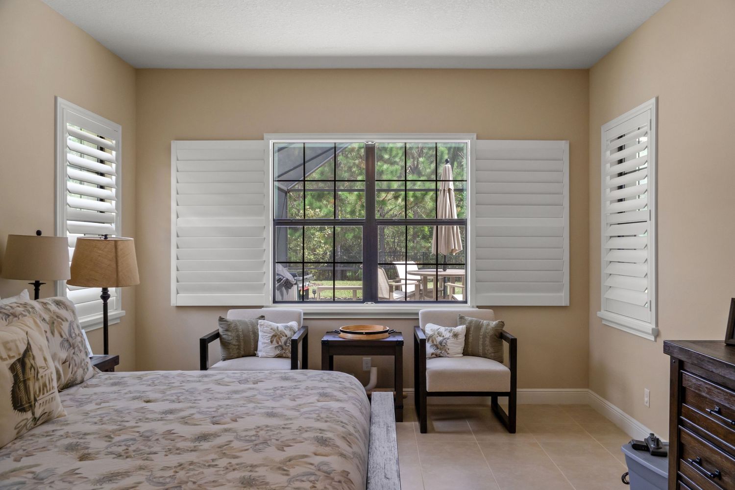 Neutral-toned living space with large windows, plantation shutters, and minimal furnishings.