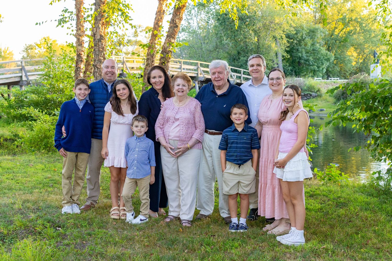 Extended family poses in coordinated pastel outfits gather outdoors for a family photo session near North Bridge in Concord, MA.