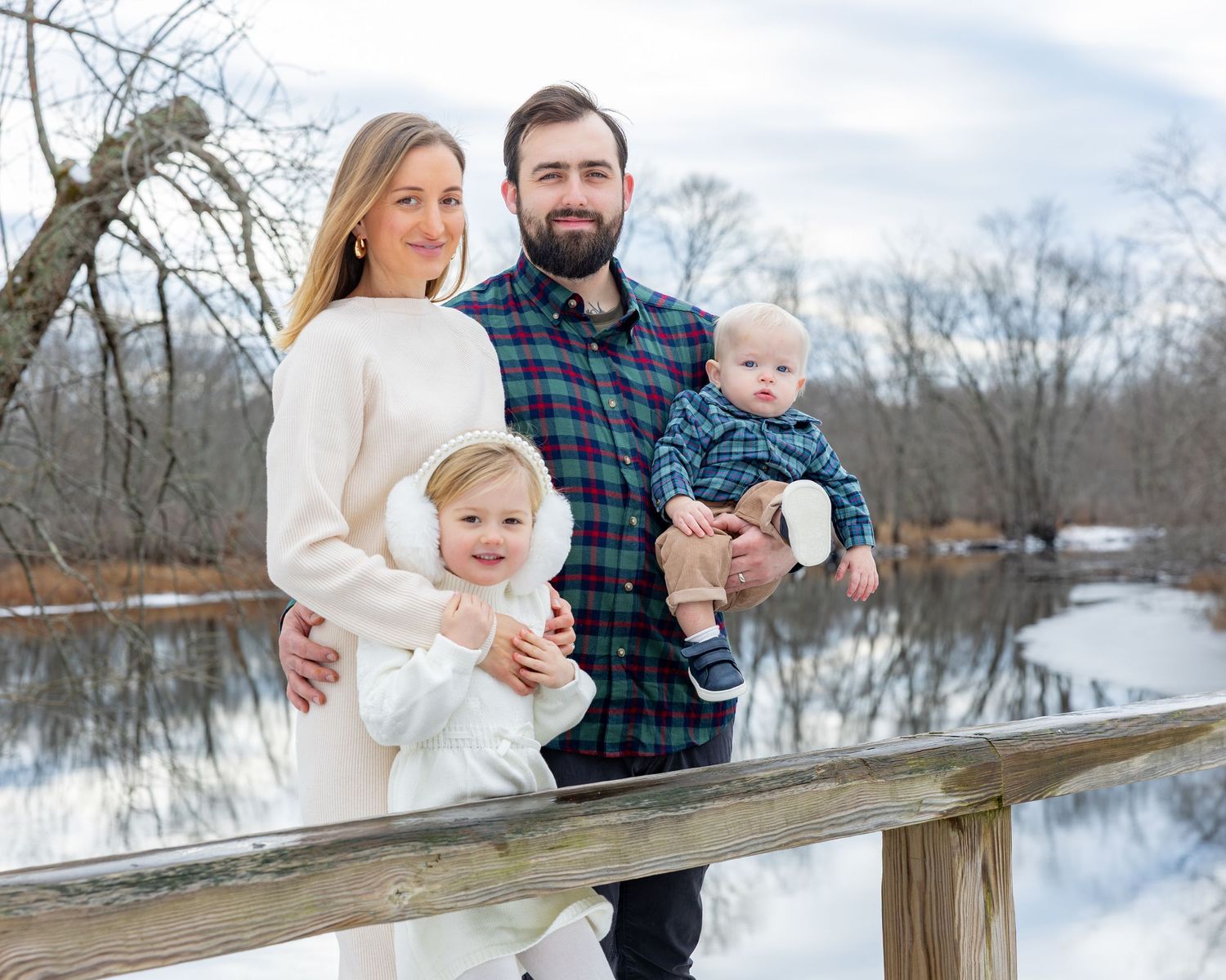 Family of four stands on North Bridge overlooking Concord River in a wintery landscape during their family photography session in Concord.