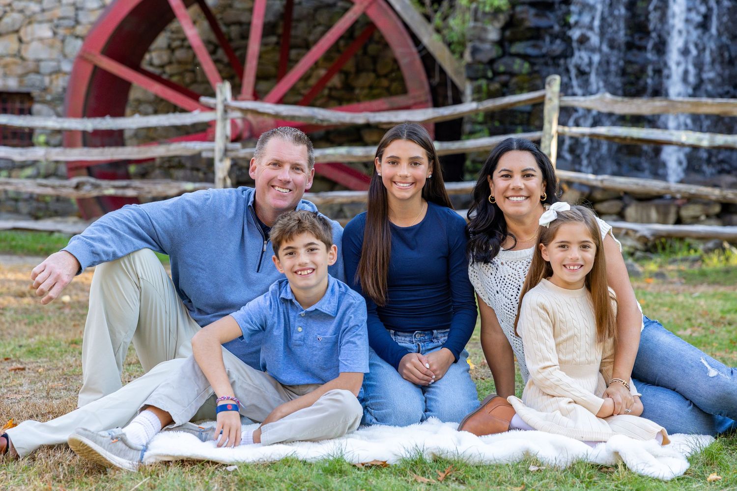 Family sits on grass and poses together at Wayside Inn Grist Mill in Sudbury, MA during their family photography session.