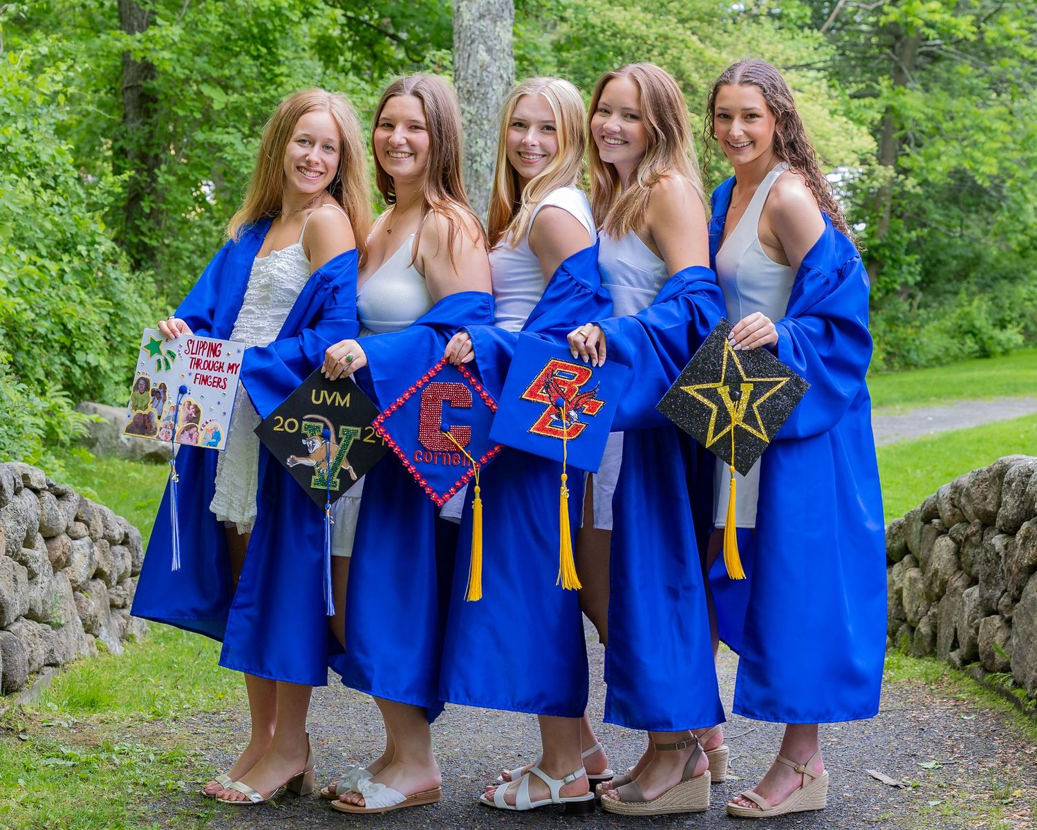 Graduates in royal blue show off their decorated mortar boards while posing together outdoors during Cap and Gown photo session in Sudbury.