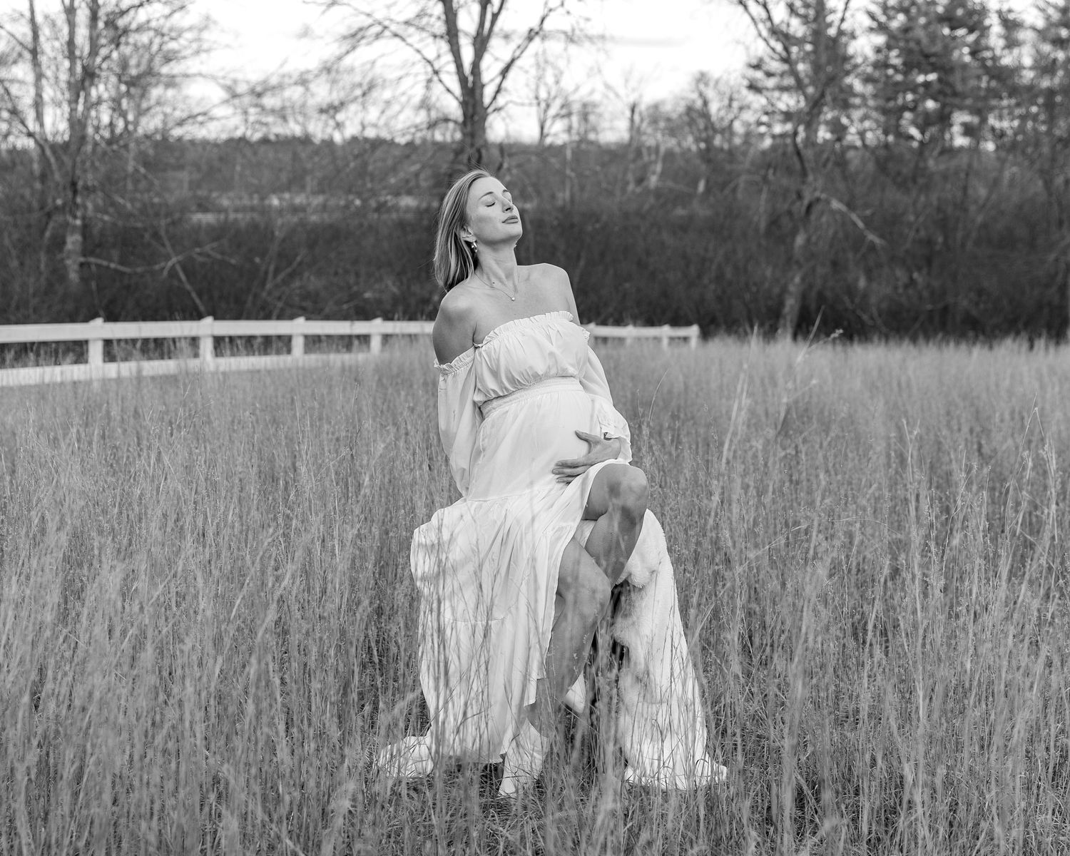 A romantic black & white photo of a pregnant woman during a maternity photo shoot in a rustic outdoor field setting in Sudbury, MA.