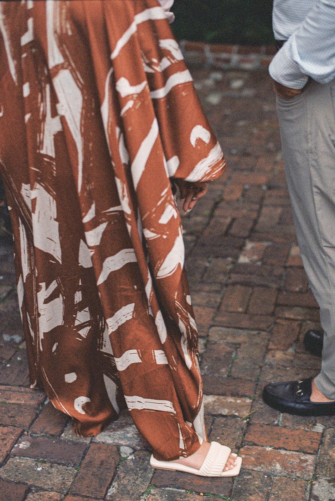 Close-up of brown and white patterned dresses and formal wear against brick pavement.