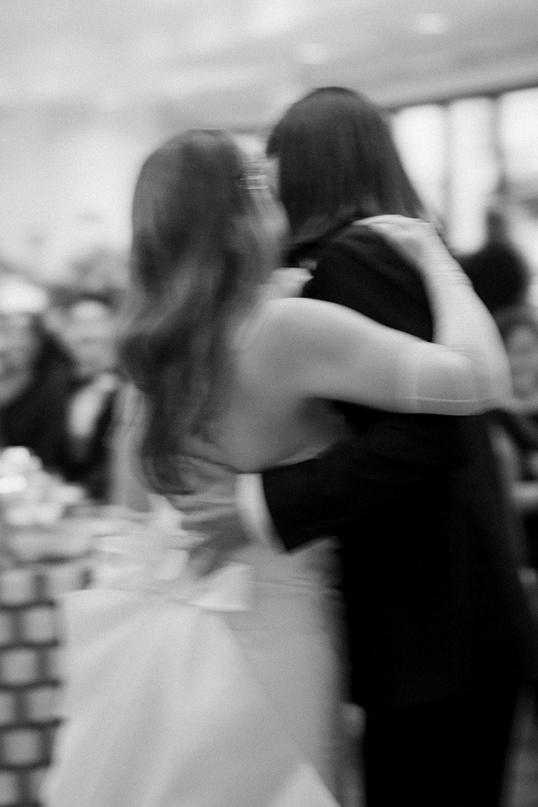 Motion blurred black and white photo of couples dancing at an elegant indoor event.