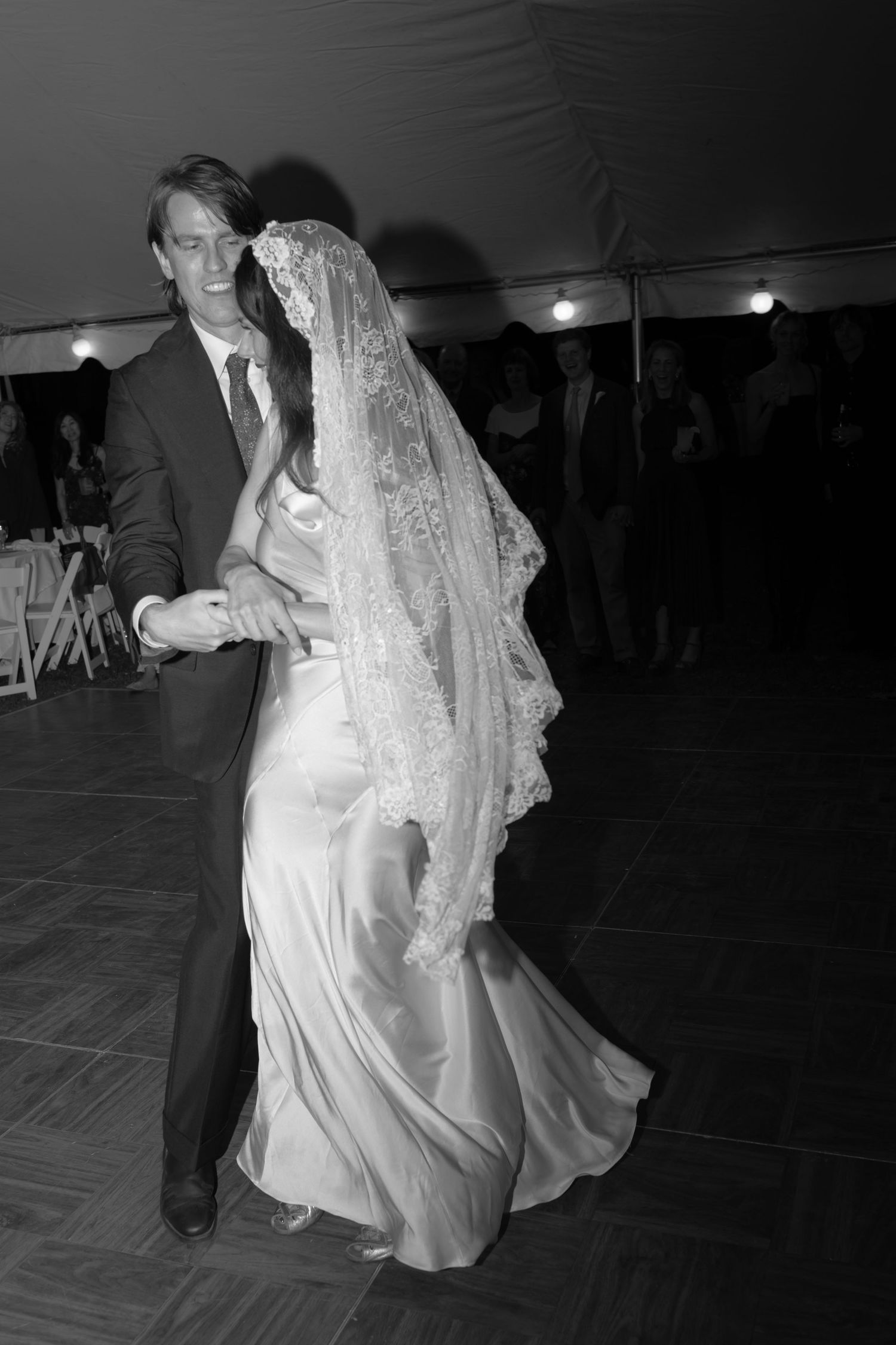 A couple shares their first dance at a wedding reception, with the bride wearing a flowing white gown and lace veil.