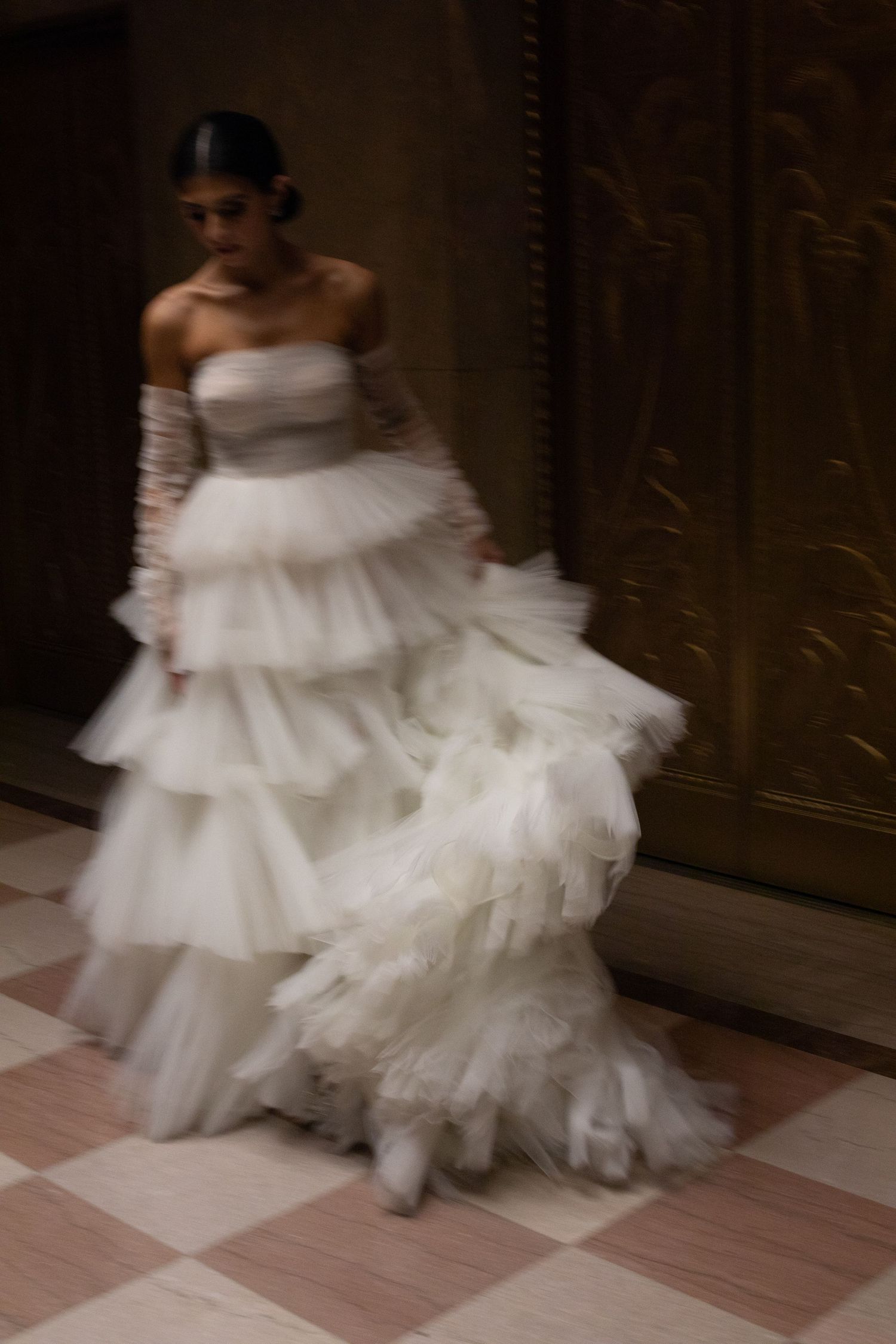 A flowing white wedding dress with ruffled layers photographed in motion against a dark background.
