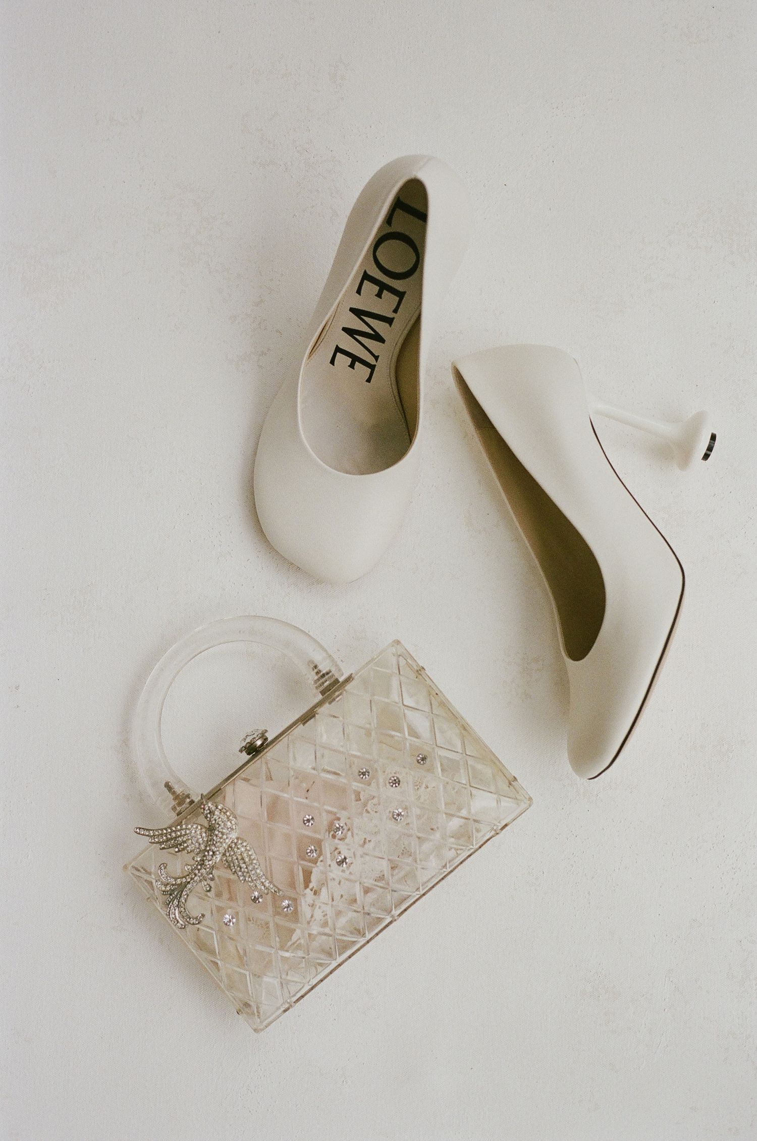 Wedding clutch purse with delicate beaded design and intricate lace pattern sits elegantly beside white bridal shoes.
