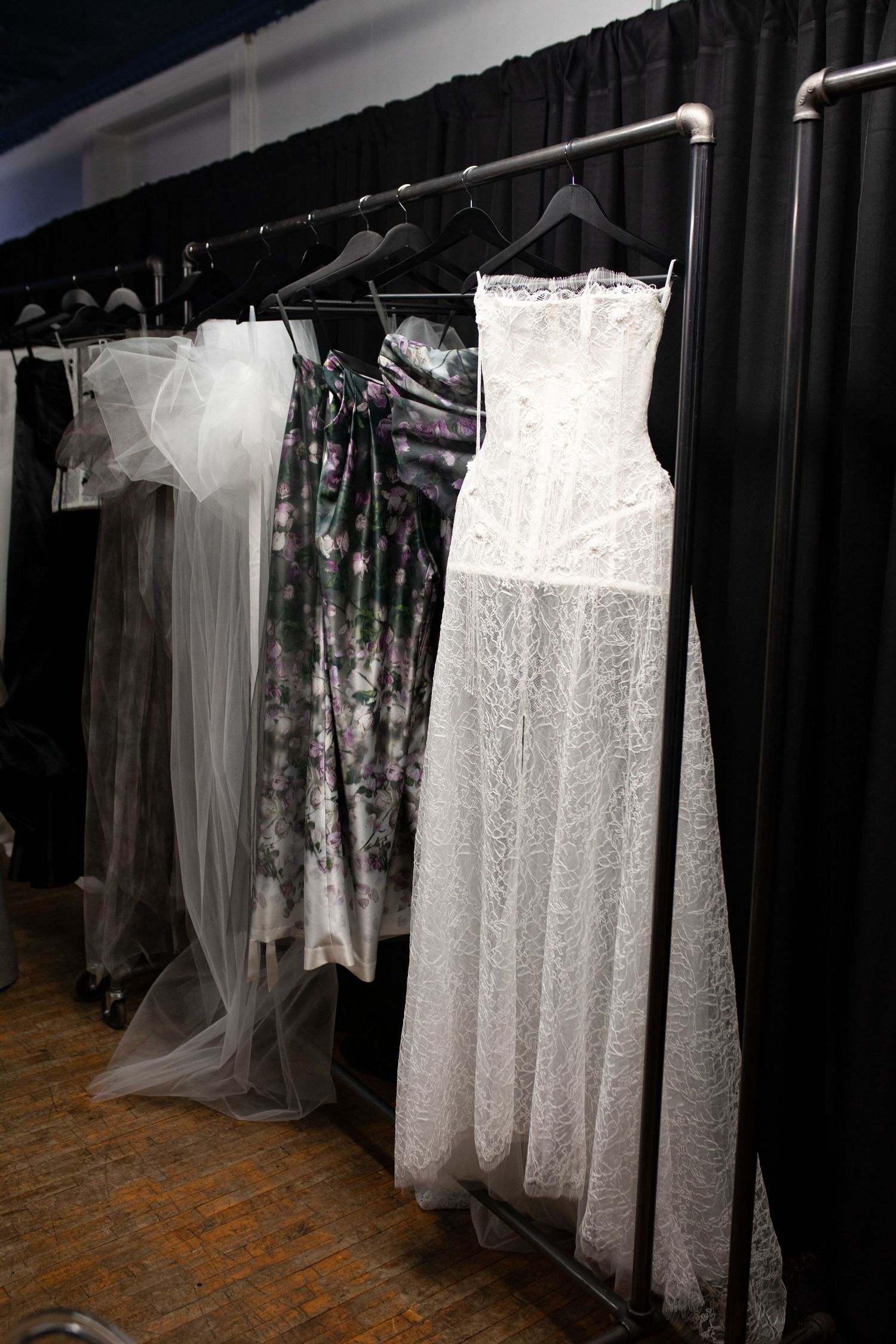 Wedding dresses and formal gowns displayed on hangers against a black curtain backdrop in a bridal shop.