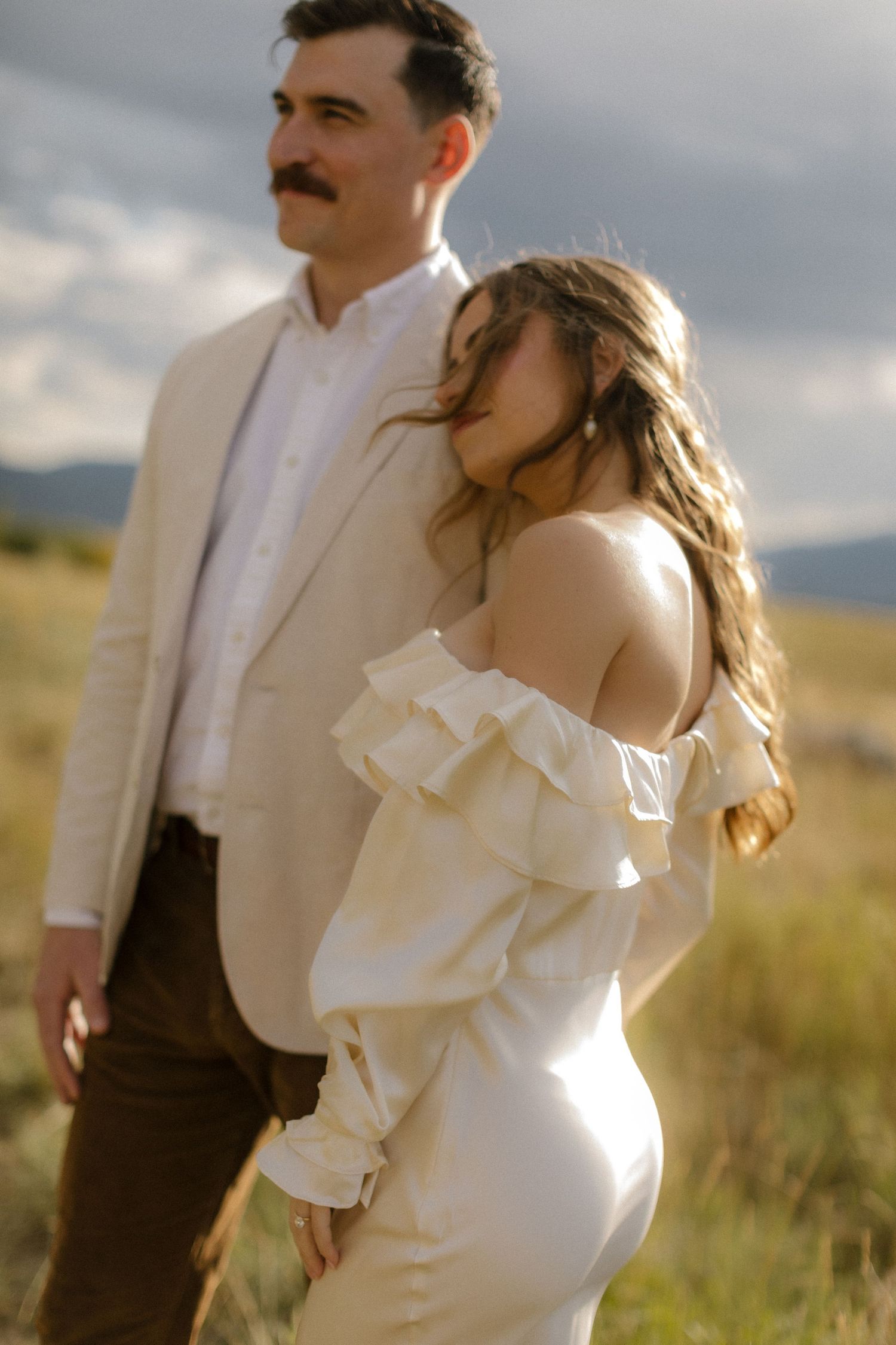 A romantic couple embraces in a sun-drenched field with golden light illuminating their wedding attire.