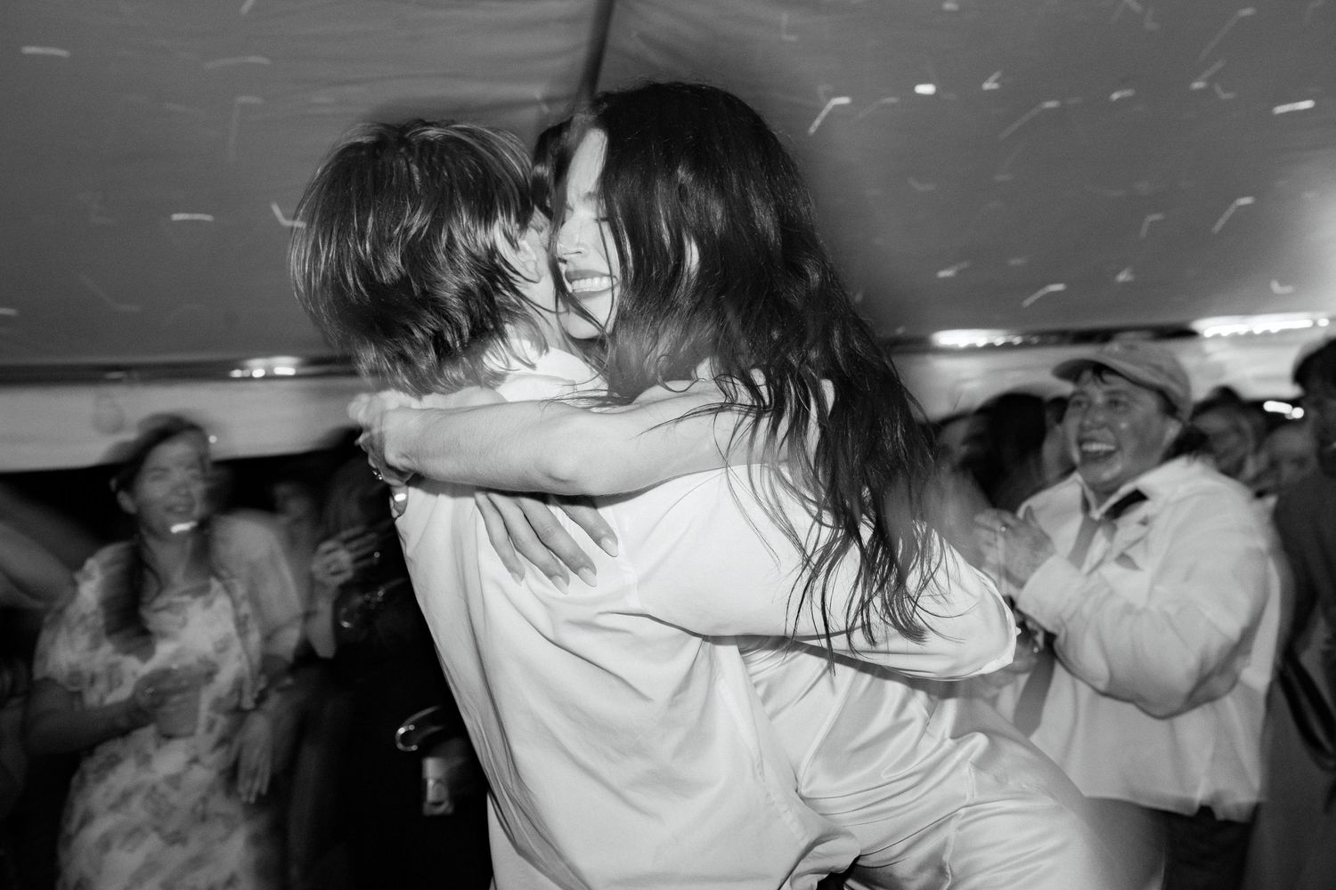 Black and white photo of a joyful couple embracing and dancing at a wedding reception under a tent.