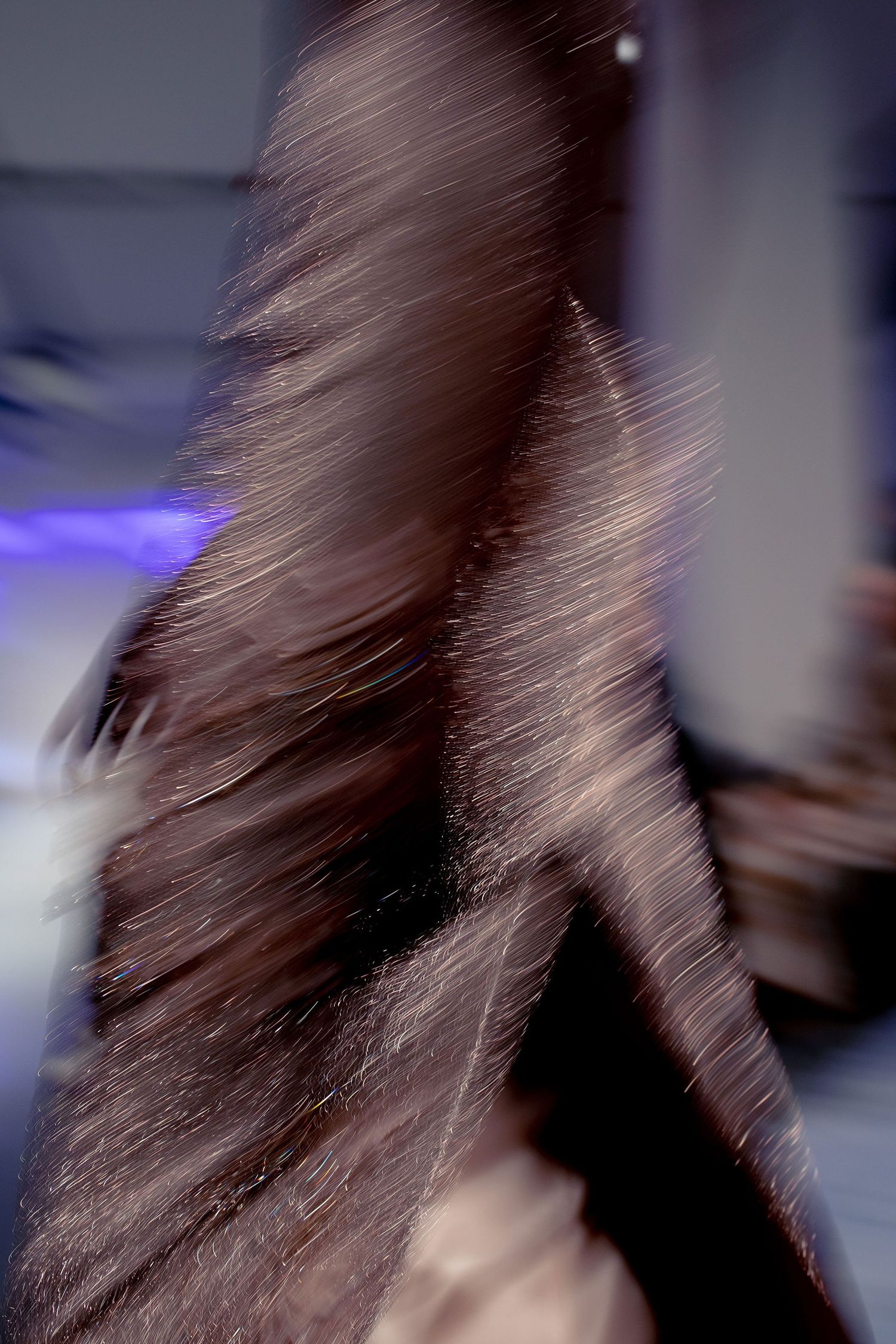 Blurred motion shot of flowing brown hair against a dark background with purple lighting.