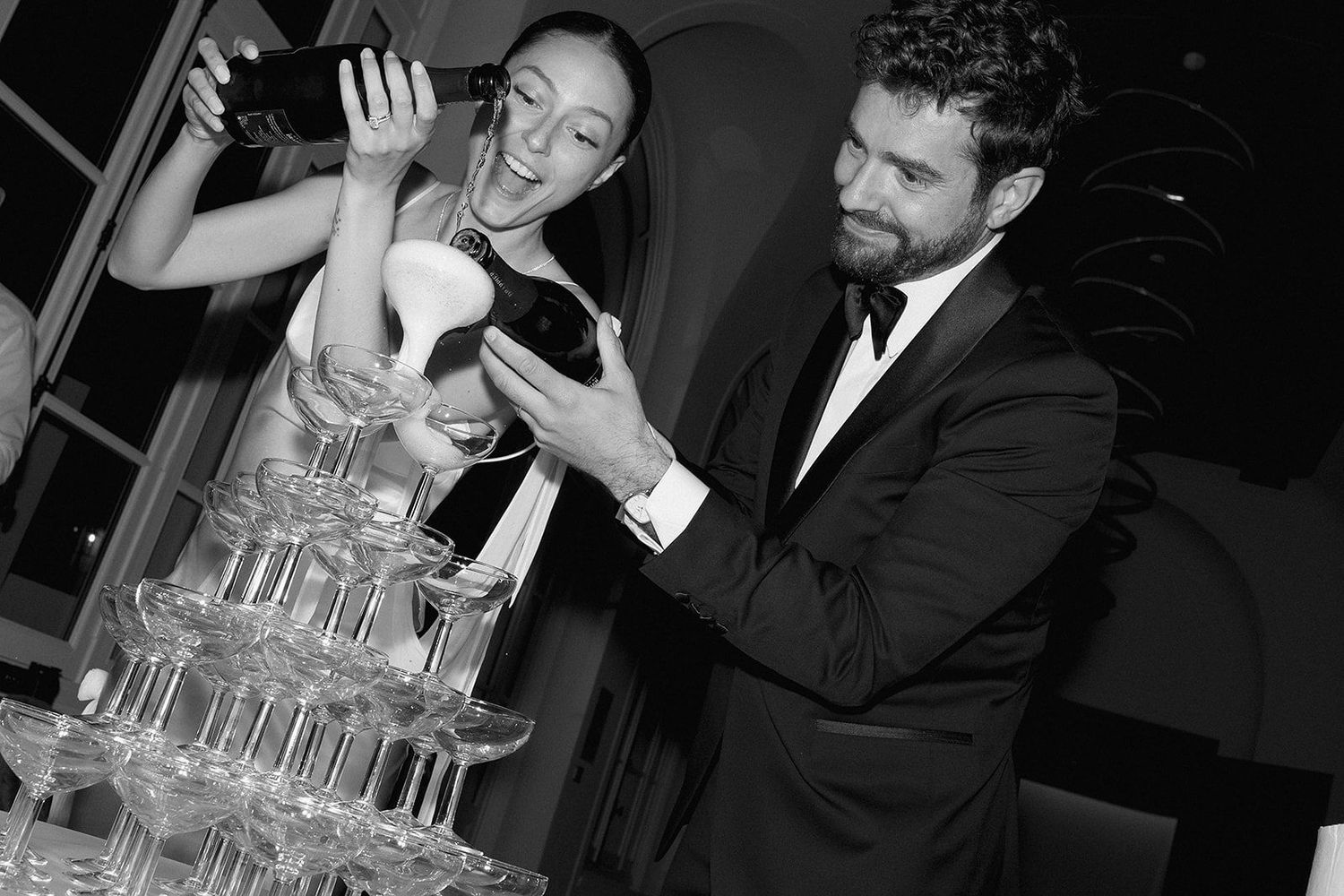 A group of people laughing and socializing at an elegant event with champagne glasses and formal attire.