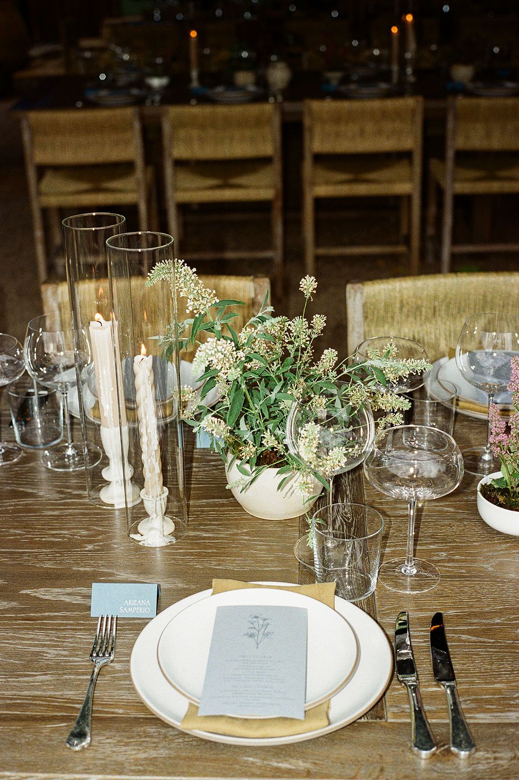 Elegant wedding table setting with floral centerpiece, taper candles, crystal glassware, and a menu card on a wooden table.