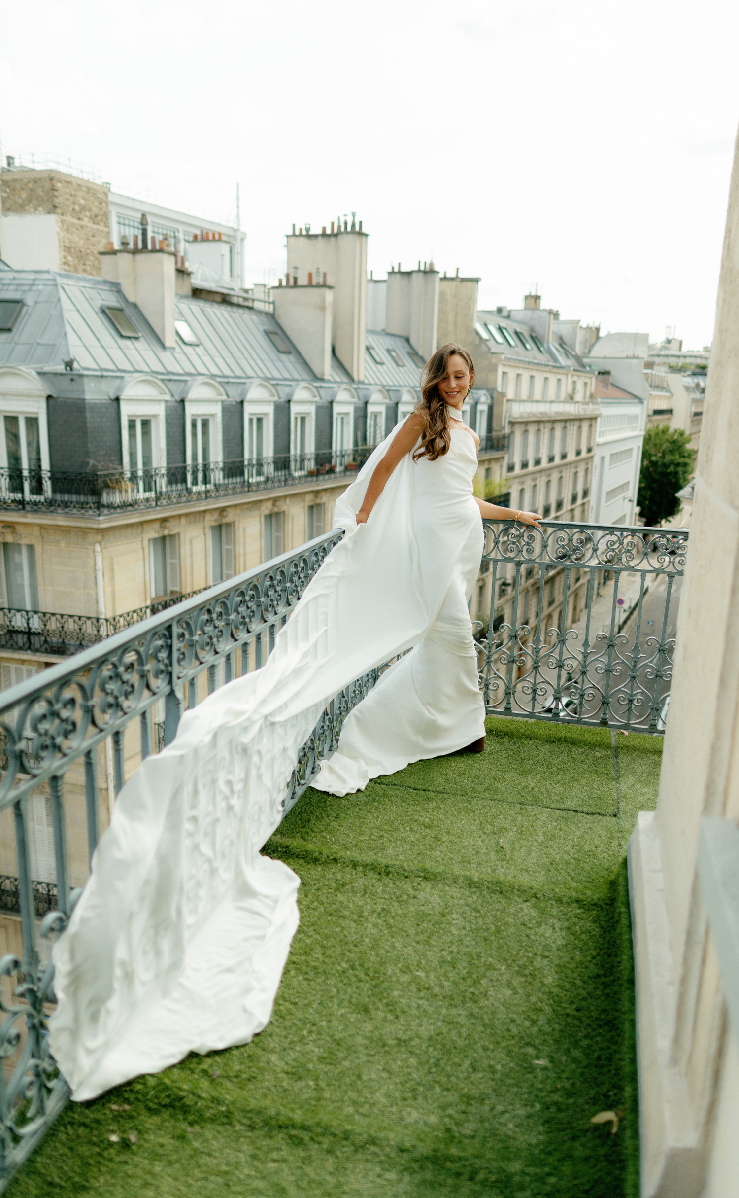 A flowing white wedding dress captured on a Parisian balcony with classic architecture.