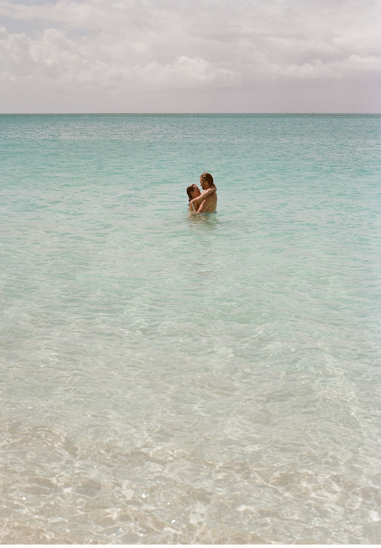 A romantic couple embracing in crystal clear turquoise ocean waters under cloudy skies.