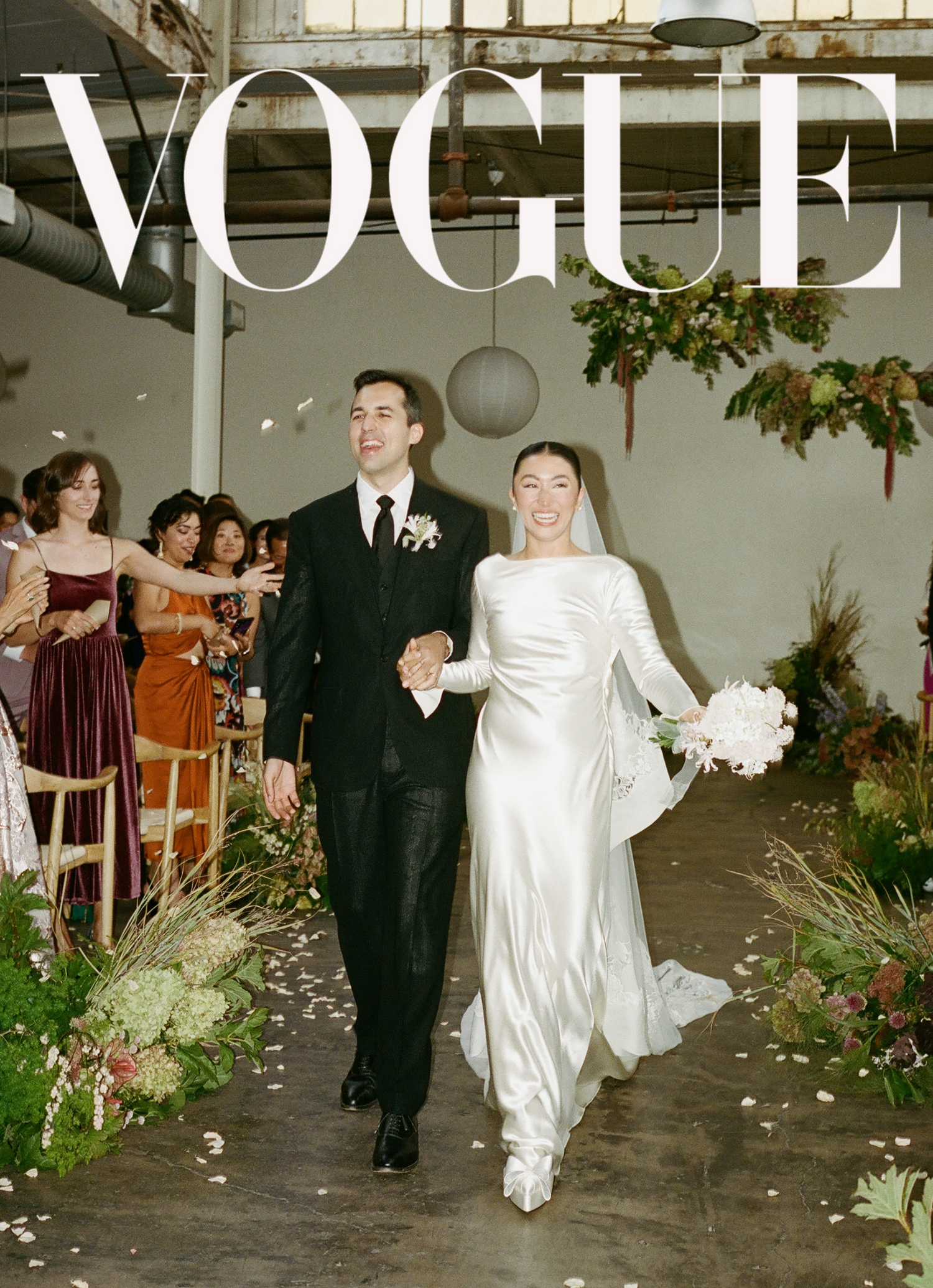 Wedding photo of couple walking down greenery-lined aisle with Vogue magazine branding.