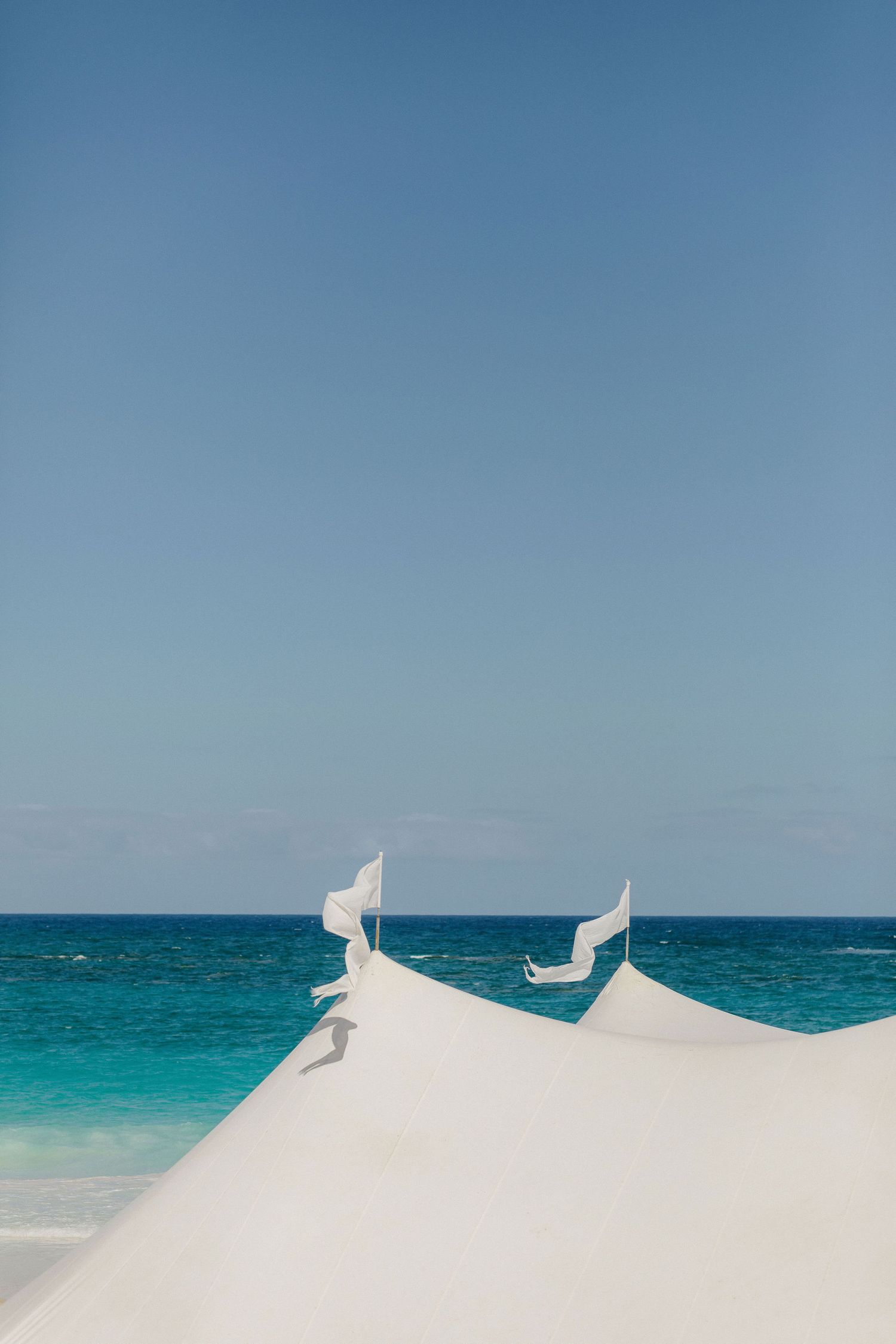 Panoramic view of pristine turquoise ocean waters meeting white sand beach under clear blue sky.