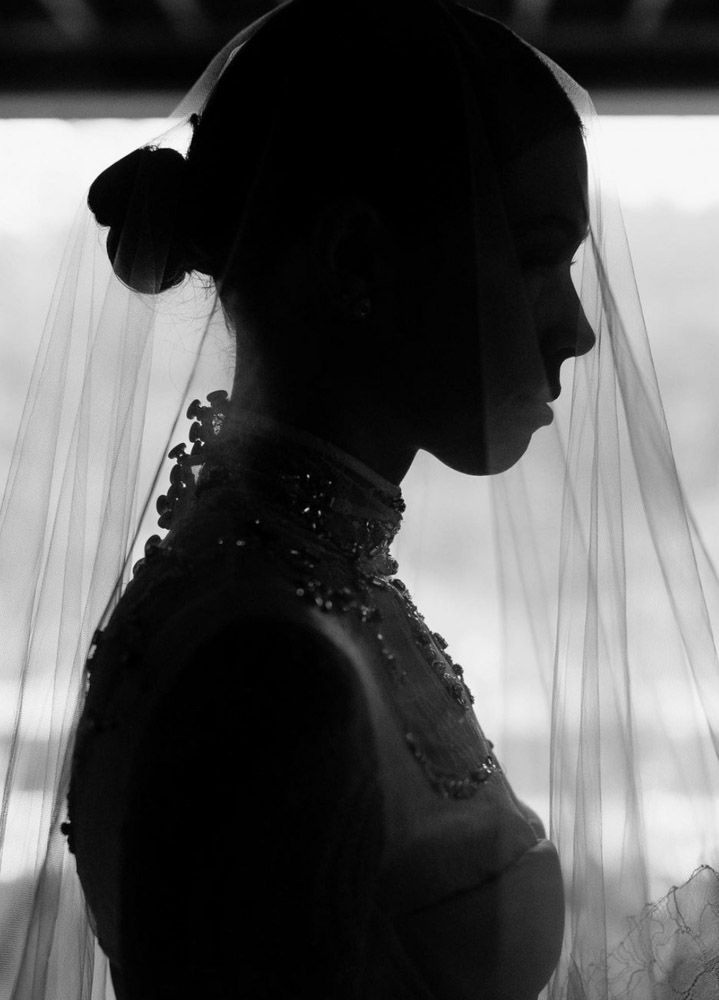 Black and white silhouette of a bride in a veil and beaded gown, photographed in profile against a bright window.