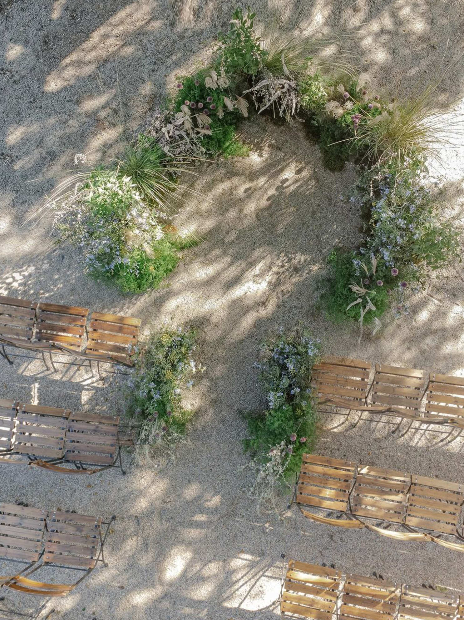 Aerial view of wooden chairs arranged under a floral arch for an outdoor wedding ceremony.
