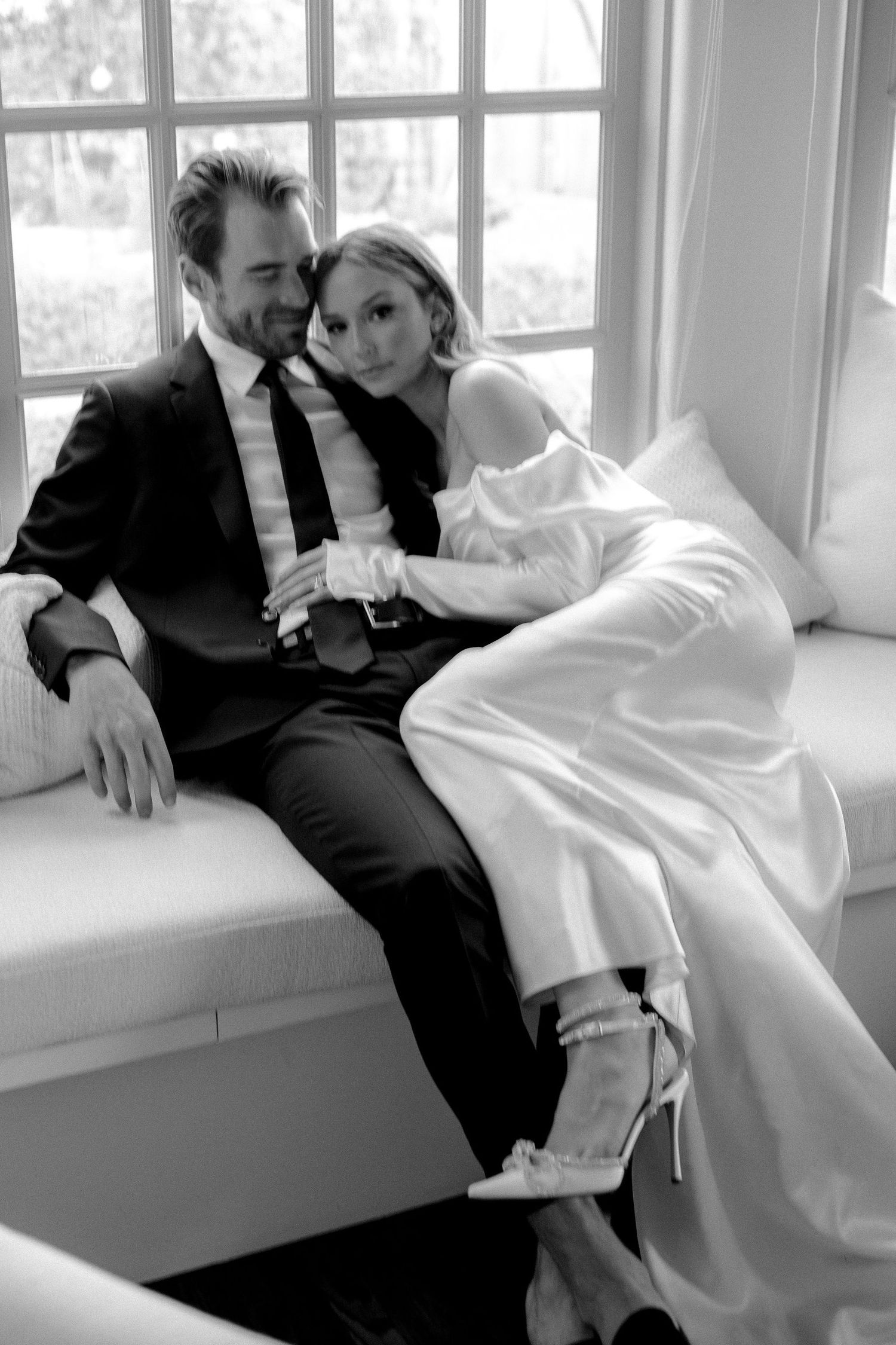 Black and white romantic photo series of a couple lounging on a windowsill in formal attire.