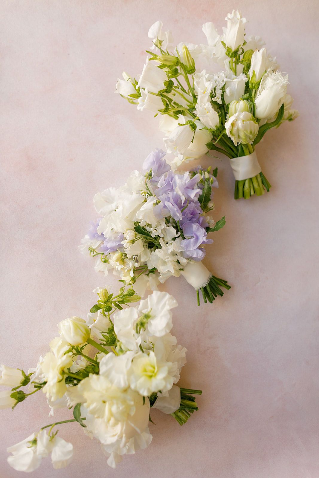 A series of delicate white and purple floral arrangements laid out in a row on a pale pink background.