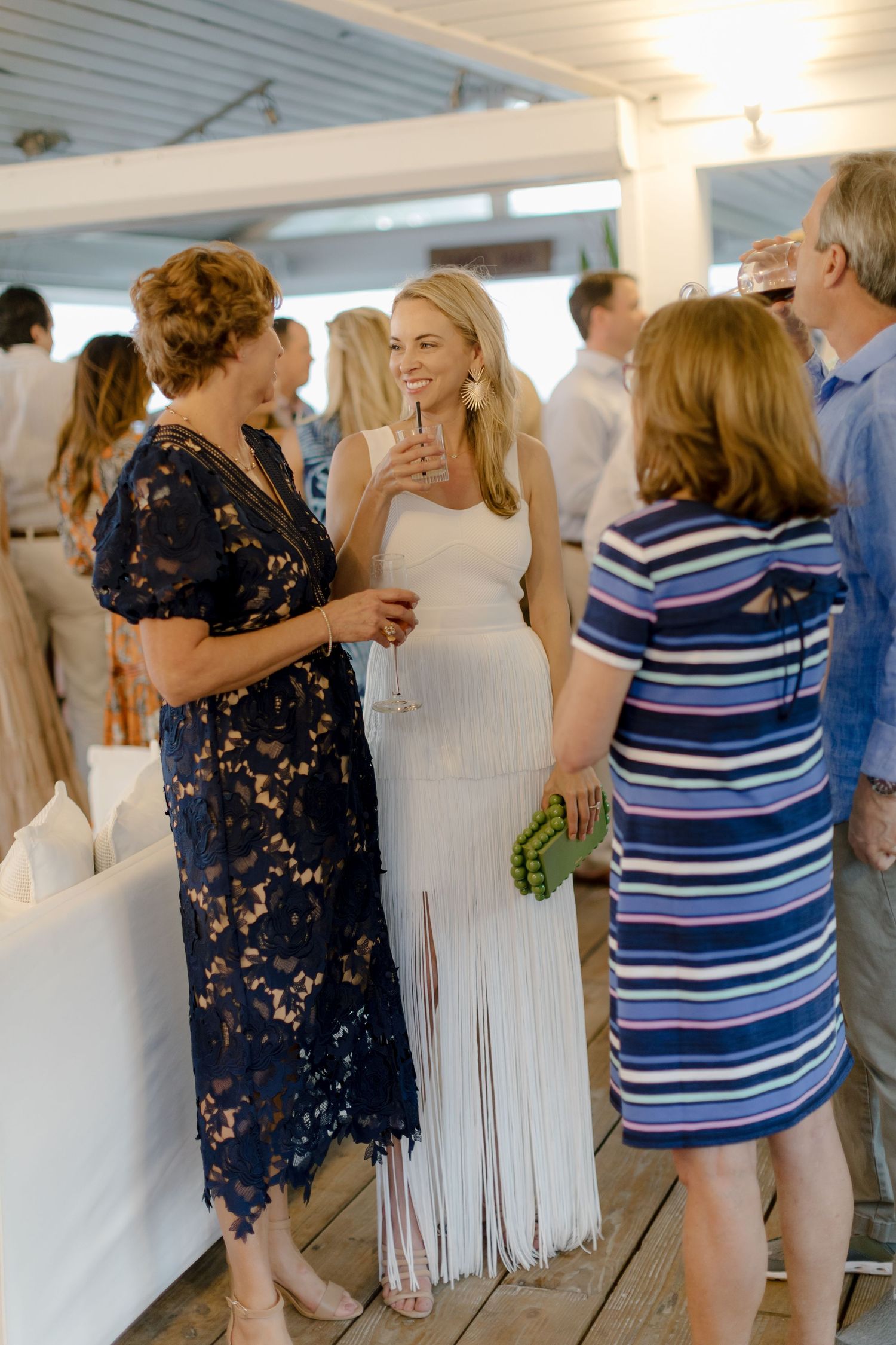 People browse and examine white dresses displayed in a brightly lit room during what appears to be a wedding dress event.