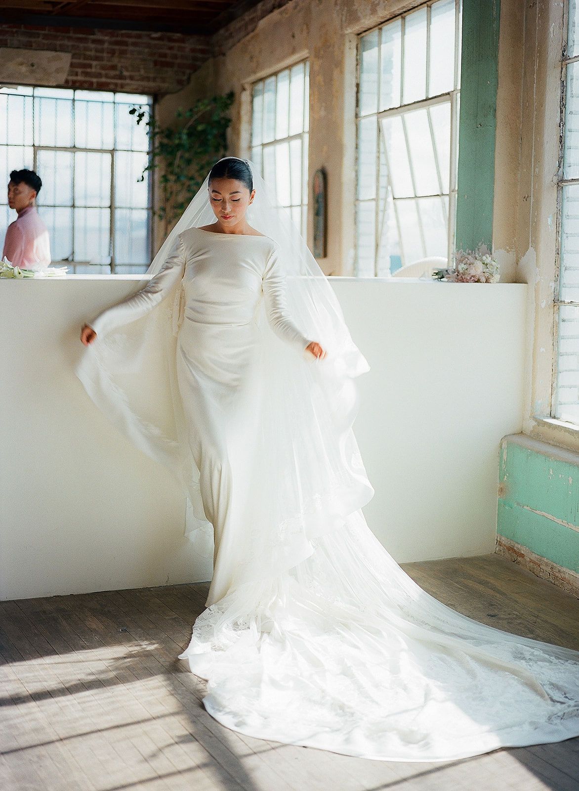 A flowing white wedding dress twirls gracefully in a bright sunlit room with large windows and wooden floors.