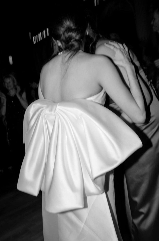 Black and white photo of a bride in a backless satin gown with large bow detail dancing at a wedding reception.
