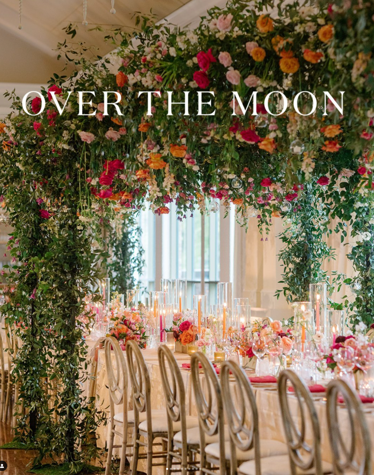 Elegant wedding reception table setup with dramatic floral arch featuring orange and pink blooms in a luxurious indoor venue.