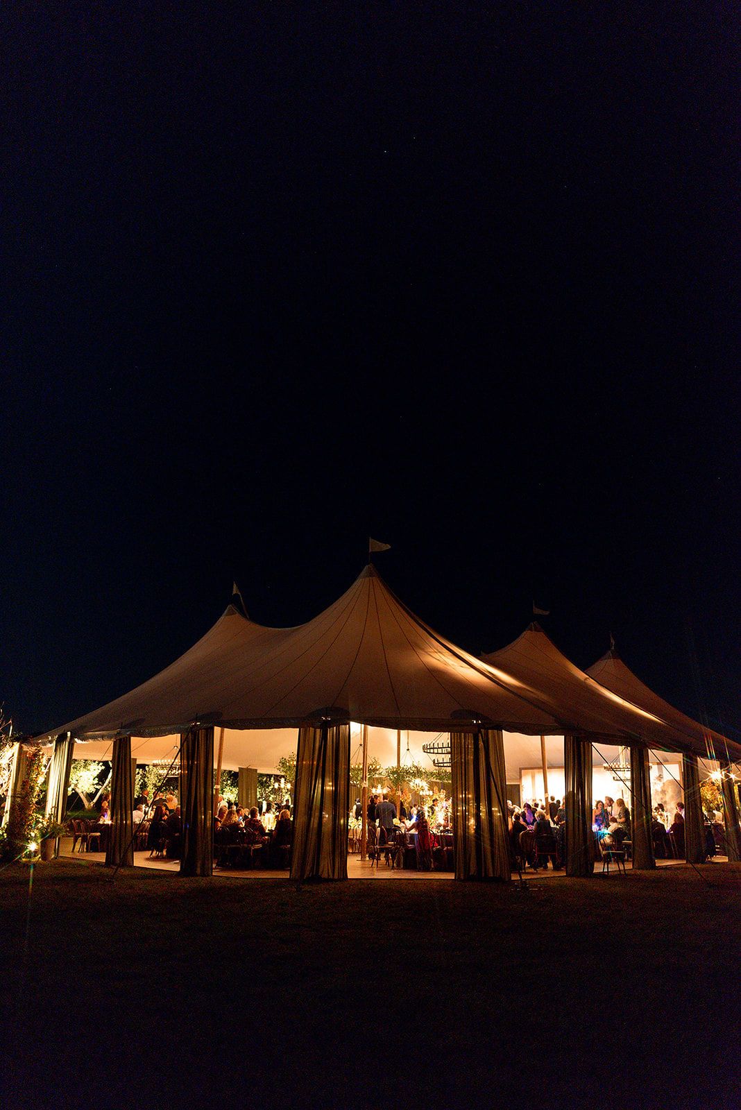 Illuminated wedding tents glowing warmly against the dark night sky at an outdoor reception venue.