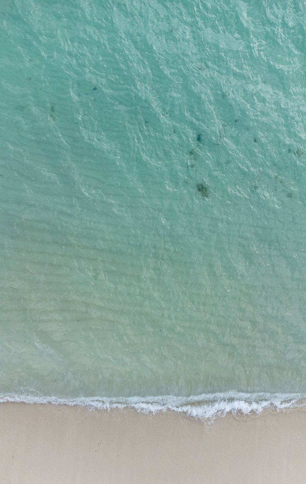 Aerial view of turquoise ocean waves gently meeting a pristine white sandy beach on a tropical shoreline.
