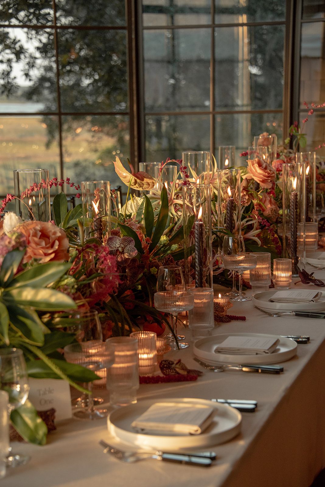 Elegant wedding reception table setting with candlelight and tropical greenery decorations in warm evening light.