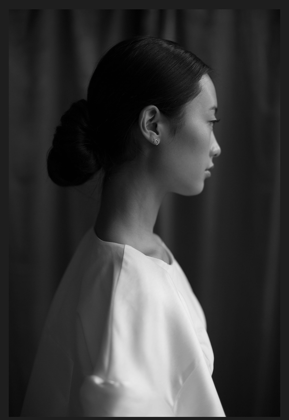 Profile view of someone in a white dress against a dark background in black and white.