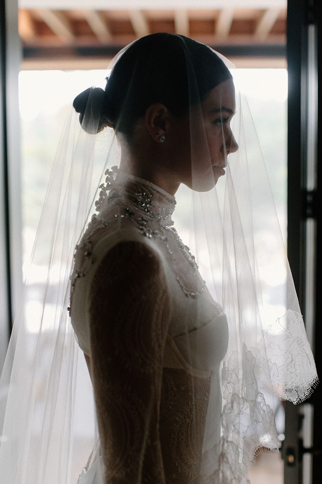 Side profile silhouette of a bride in an elegant high-necked gown with embellished details and flowing veil.