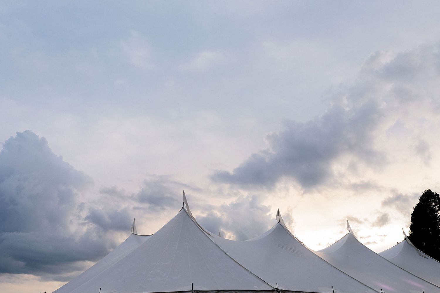 A panoramic view of white event tents against a dramatic cloudy sky at sunset.