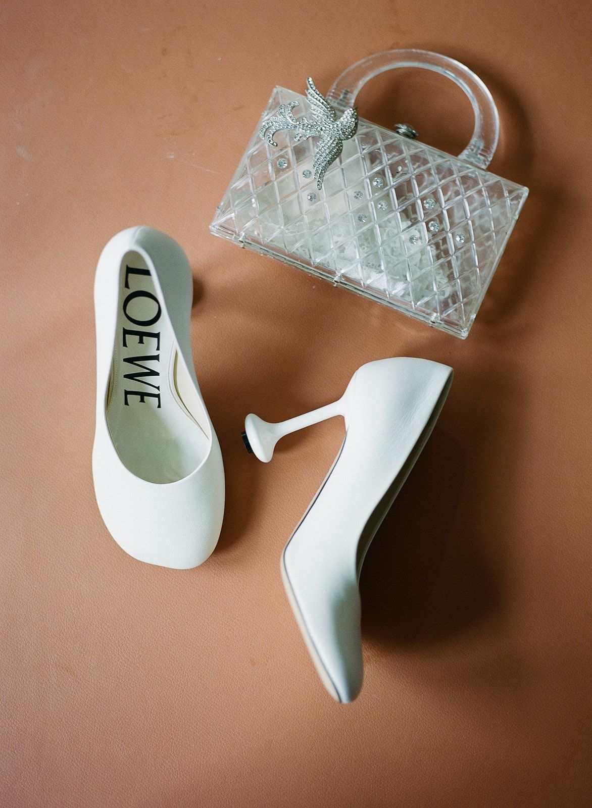 White bridal shoes and delicate crystal details arranged on a warm brown background.