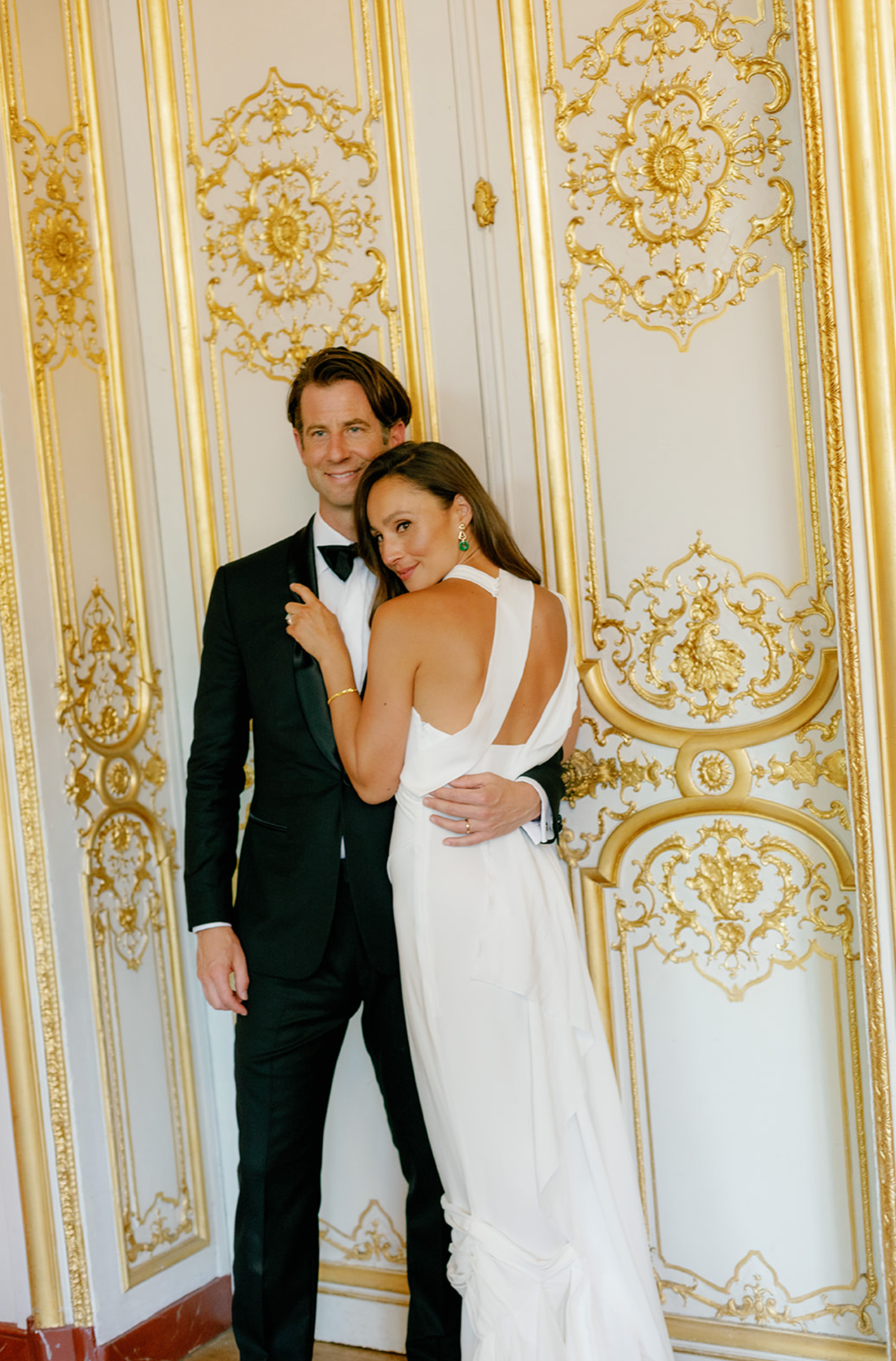 Elegant couple embraces against ornate gold and white baroque wall details.