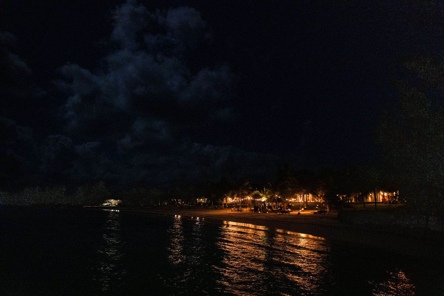A panoramic view of twinkling city lights reflected on calm water at night, creating a serene coastal nightscape.