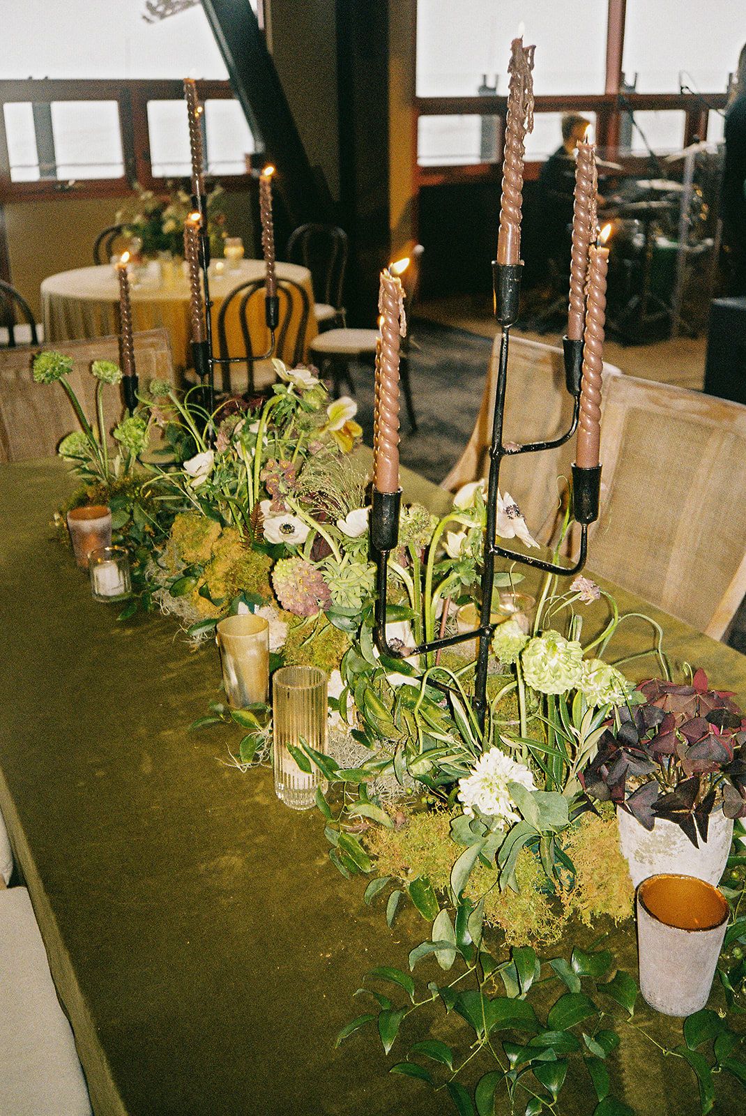Elegant table centerpiece with tall candlesticks, fresh greenery, and floral arrangements on a rustic wooden surface.