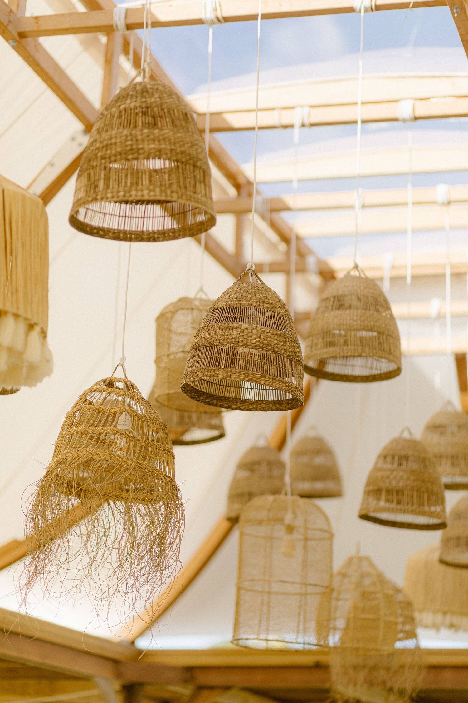 Woven basket pendant lights hang from wooden beams in a rustic bohemian style interior space.