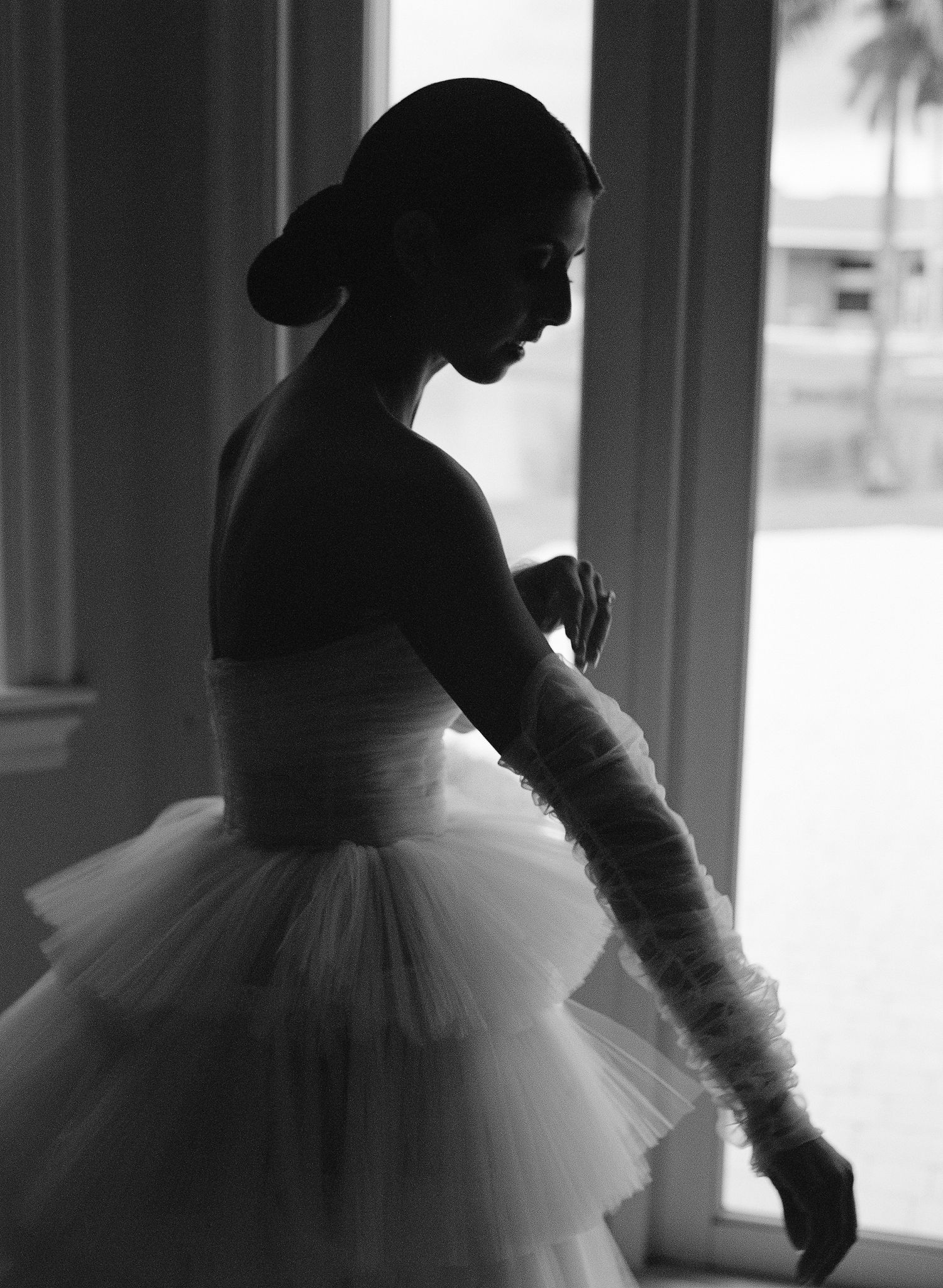 A silhouetted ballet dancer in a romantic tulle tutu poses gracefully against a bright window in black and white.