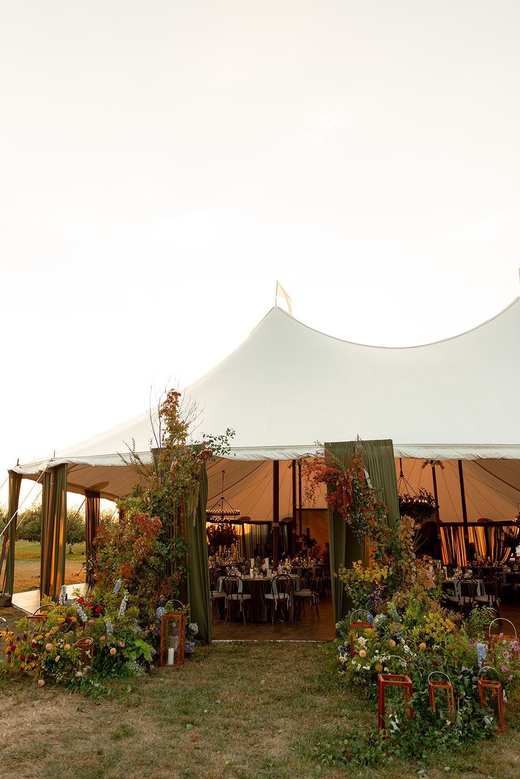 Large white wedding tent set up on grass with decorative floral arrangements and seating visible inside.
