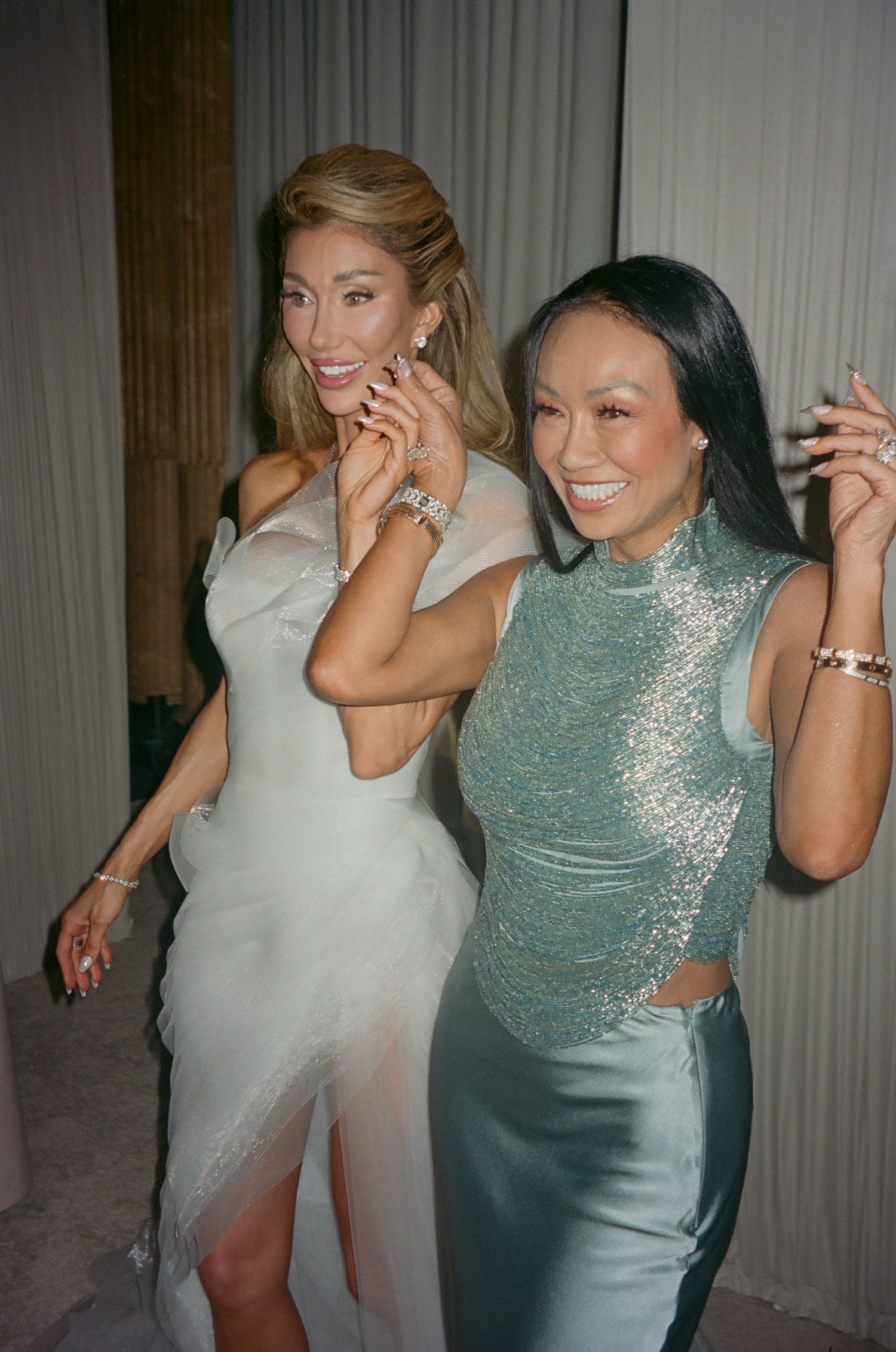 Two women in formal attire dance and laugh together during a celebration.