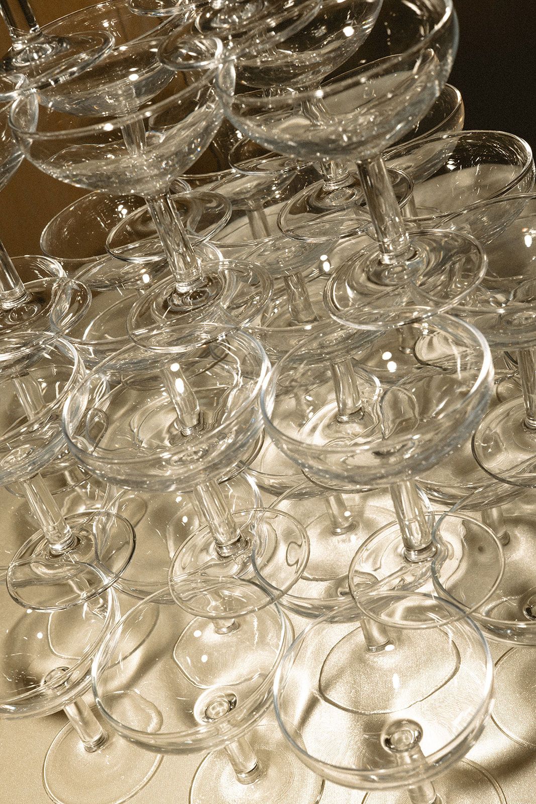Stacked crystal champagne coupes arranged in rows create an elegant pattern of glassware on a light surface.
