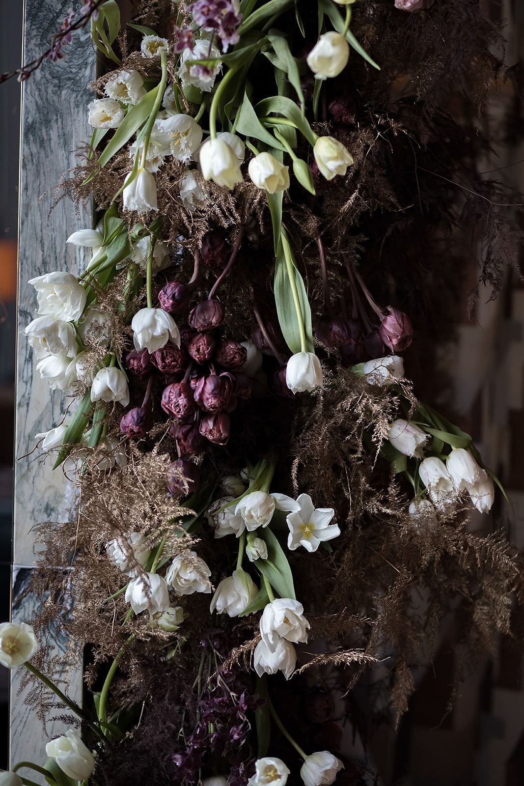 Moody floral arrangement with white tulips and dark purple blooms against a textured dark background.