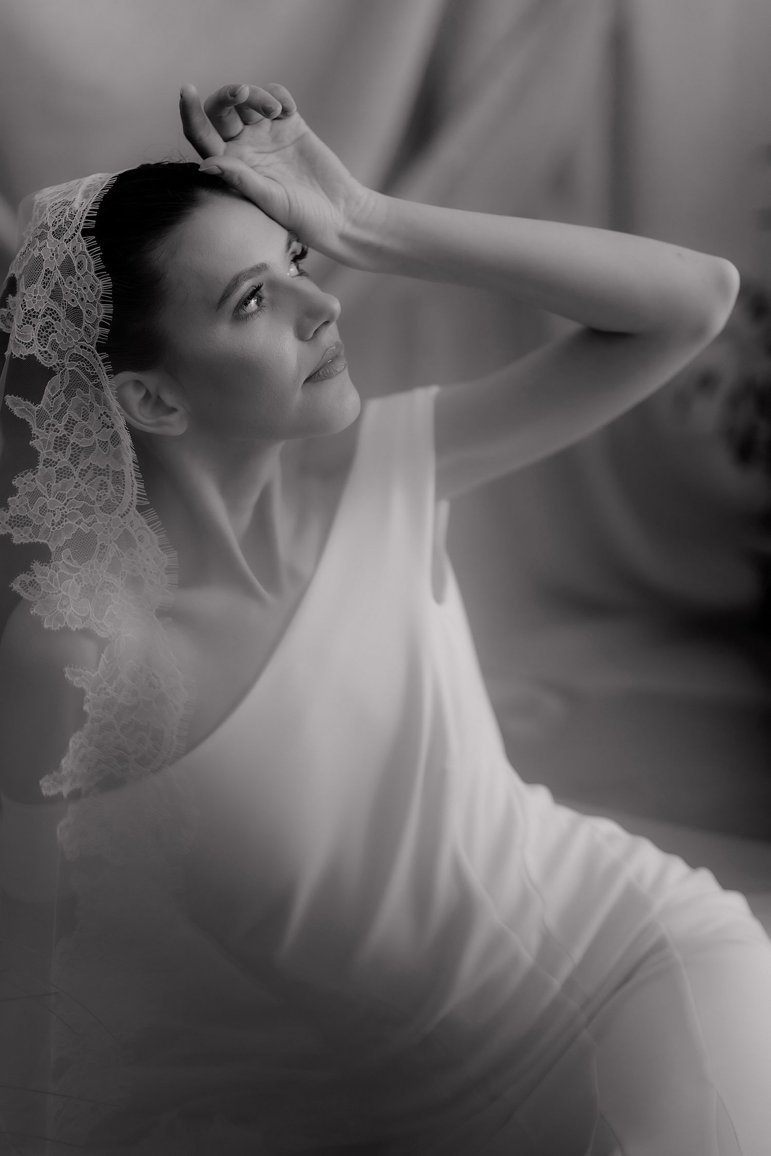 A graceful bride in a white dress and delicate veil poses in soft light during a romantic bridal portrait session.