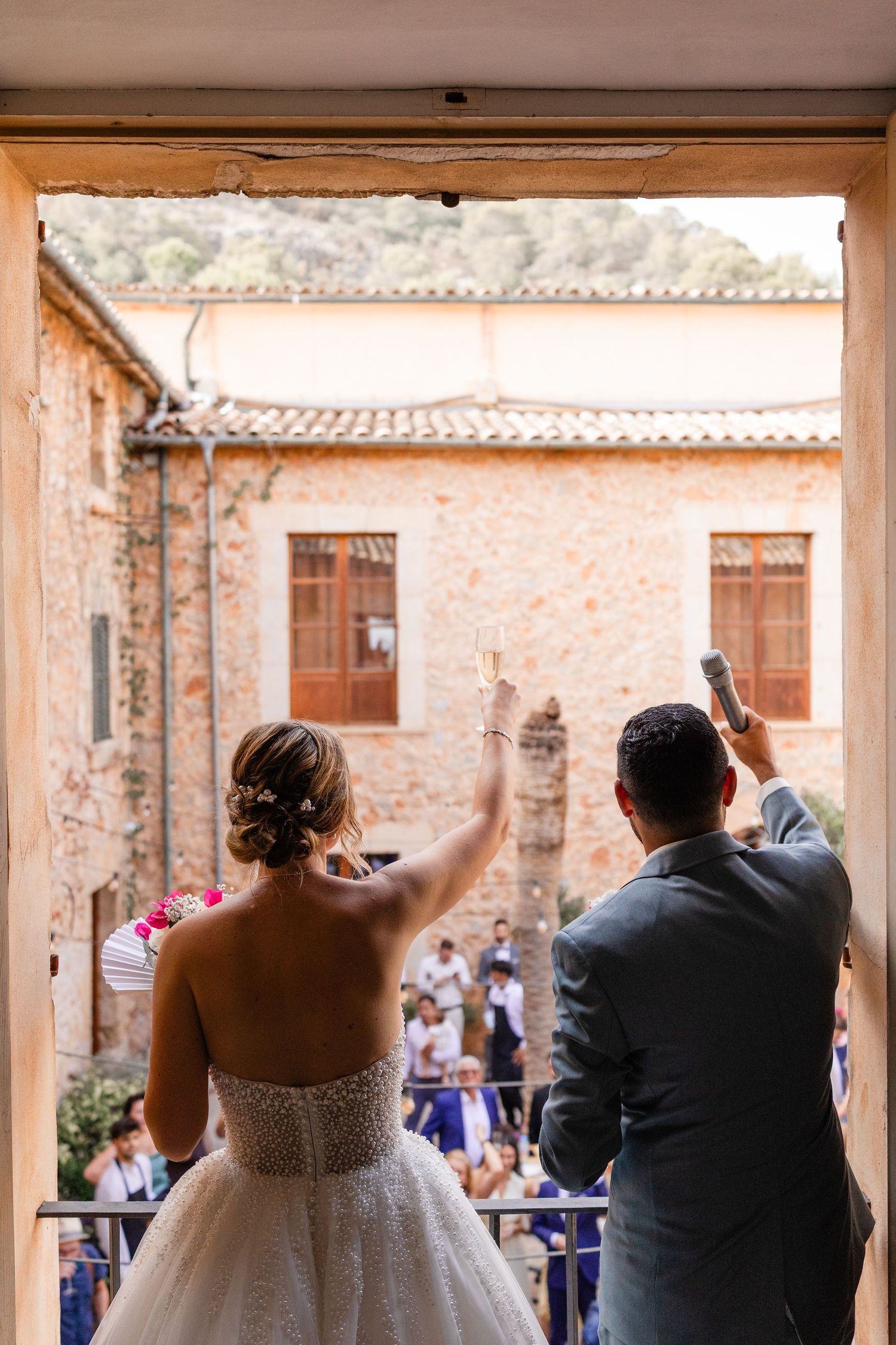 Hochzeit auf Mallorca: das Brautpaar blickt in den Innenhof der Finca mit Mikrofon und Sektglas. Foto von Reinhard A. Deutsch