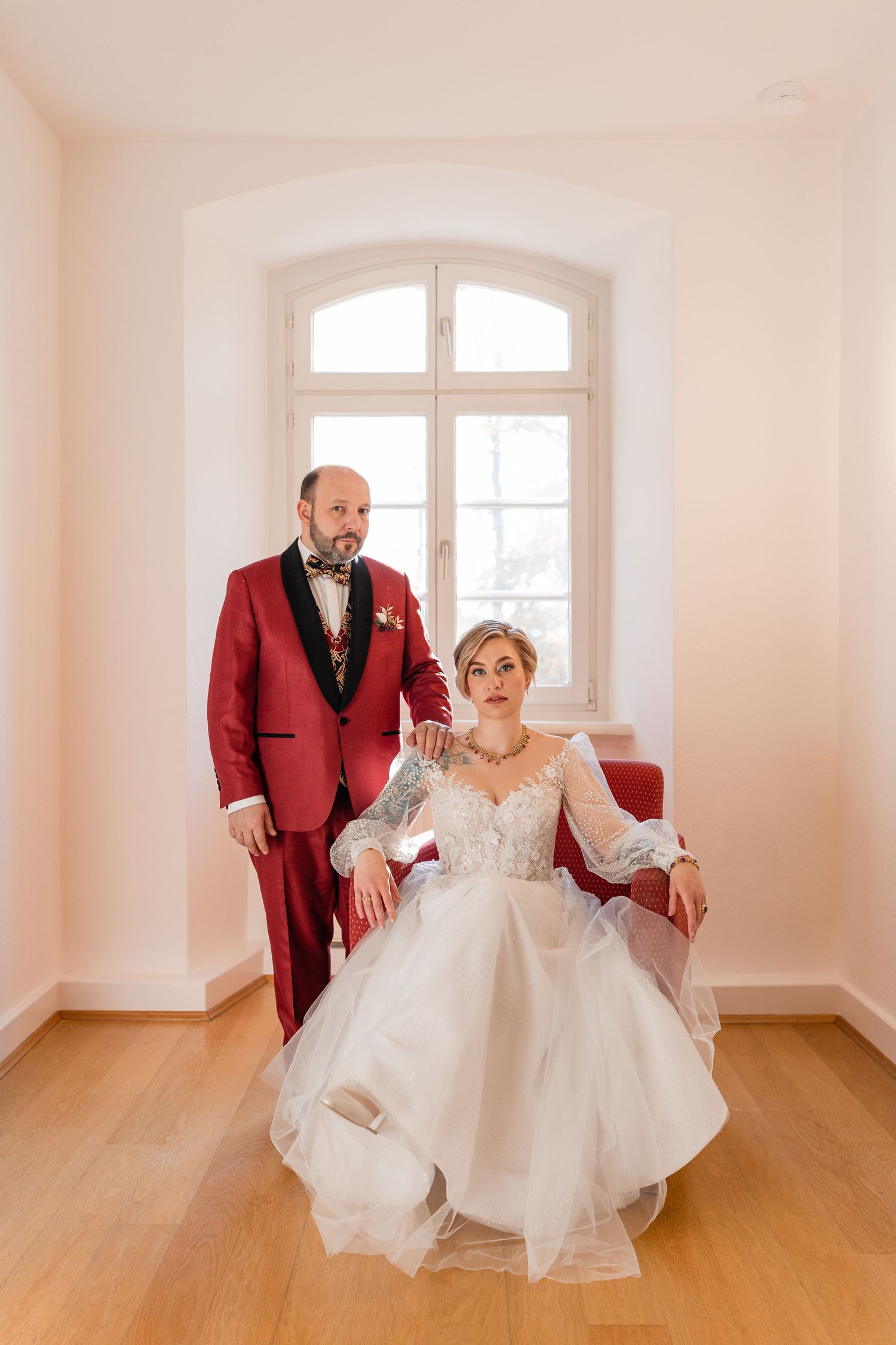 Hochzeitspaar beim Paarshooting während der Hochzeit im Klosterhotel Wötingerode, ernst in die Kamera blickend vor dem Fenster am Sessel