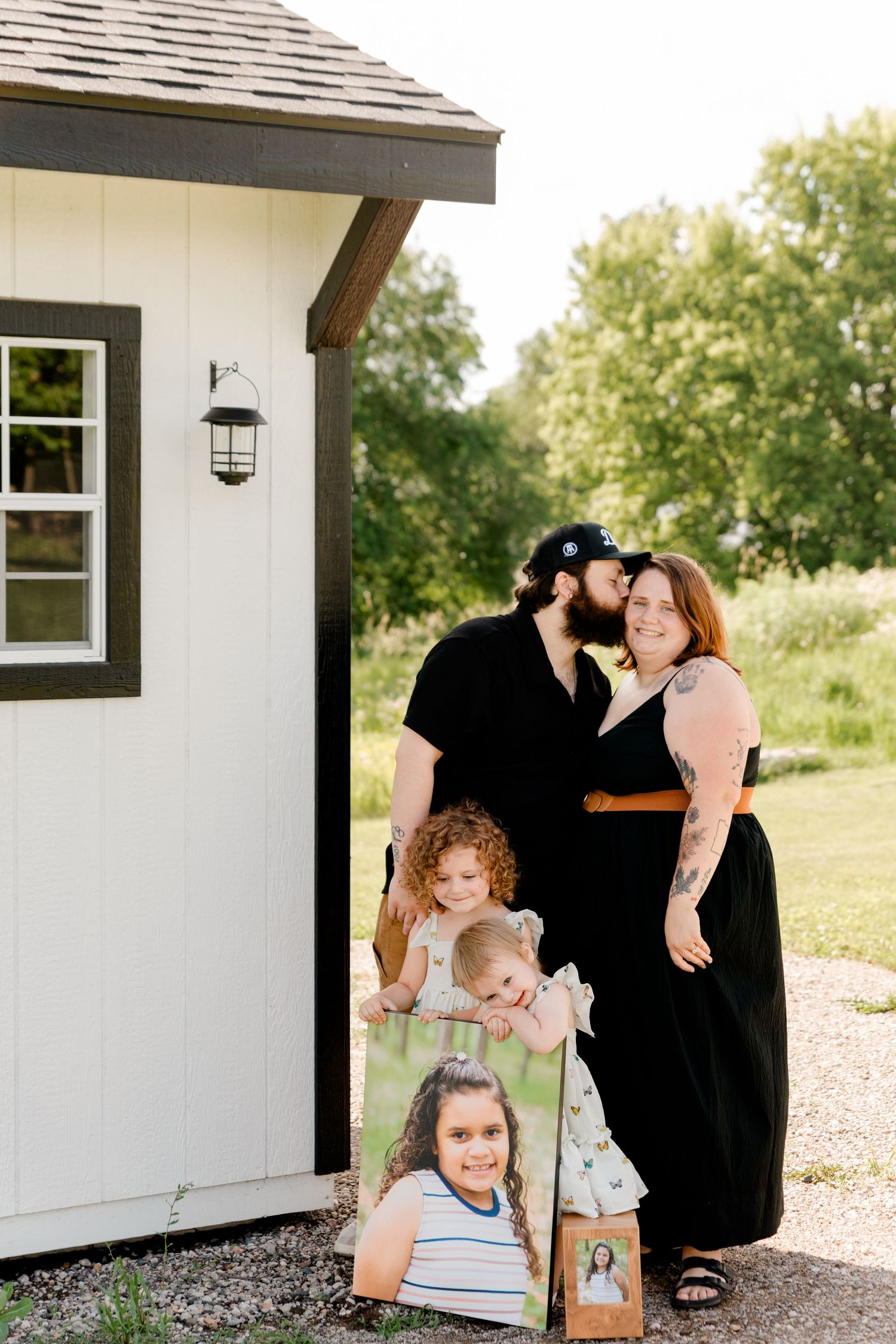 A tender family photoshoot series in black and white tones outside a modern farmhouse with white walls and black trim.
